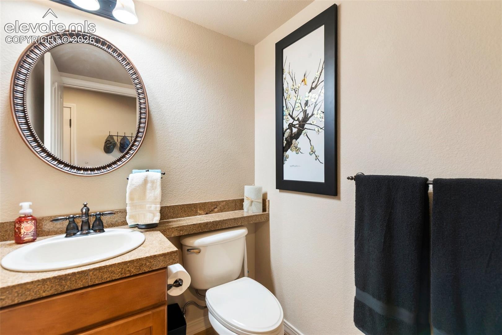 Bathroom featuring a wood-finish vanity with a stone-surfaced countertop, integrated backsplash, oval undermount sink, and decorative circular wall mirror