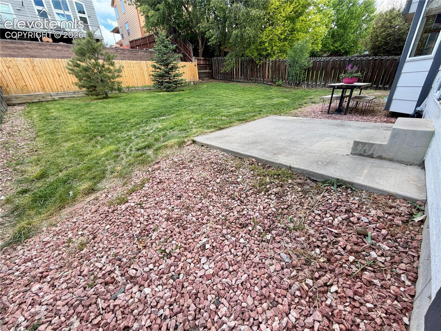 Spacious backyard with a large lawn area, trees, and a concrete patio