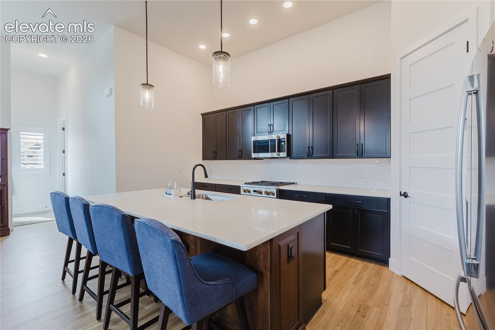 Modern kitchen featuring a 4' x 8'  island white solid countertop, dark cabinetry, stainless steel appliances