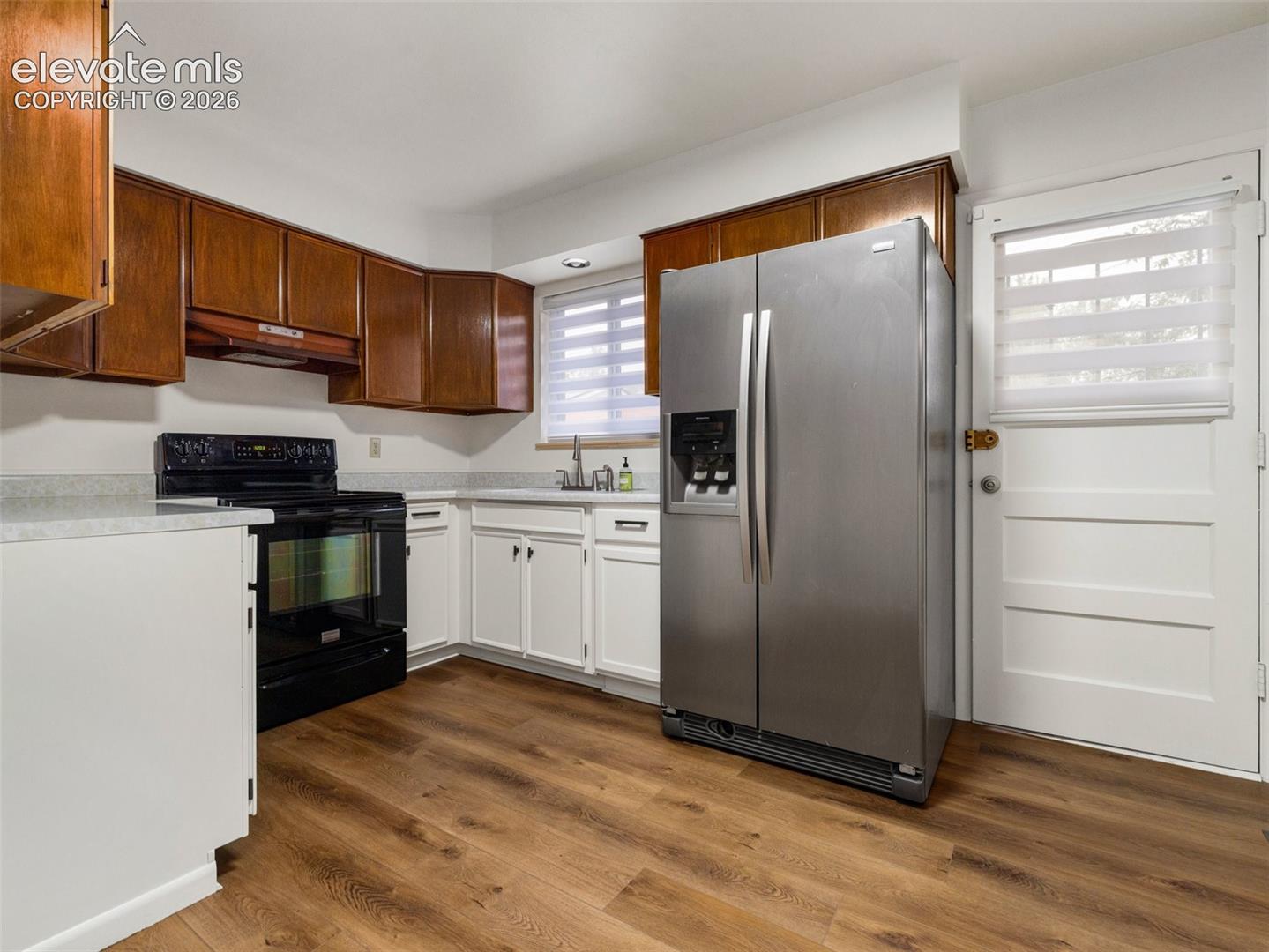 Kitchen featuring wood-finish flooring, white lower cabinetry, wood upper cabinetry, and a stainless steel refrigerator