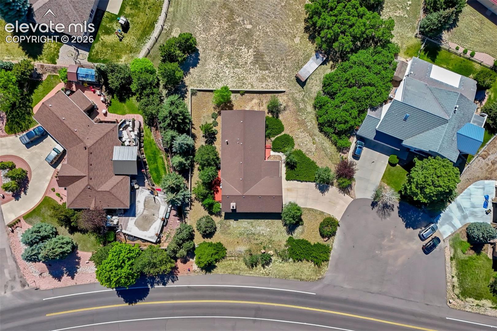 Aerial perspective showcasing a property featuring a brown shingle roof and an extensive paved driveway