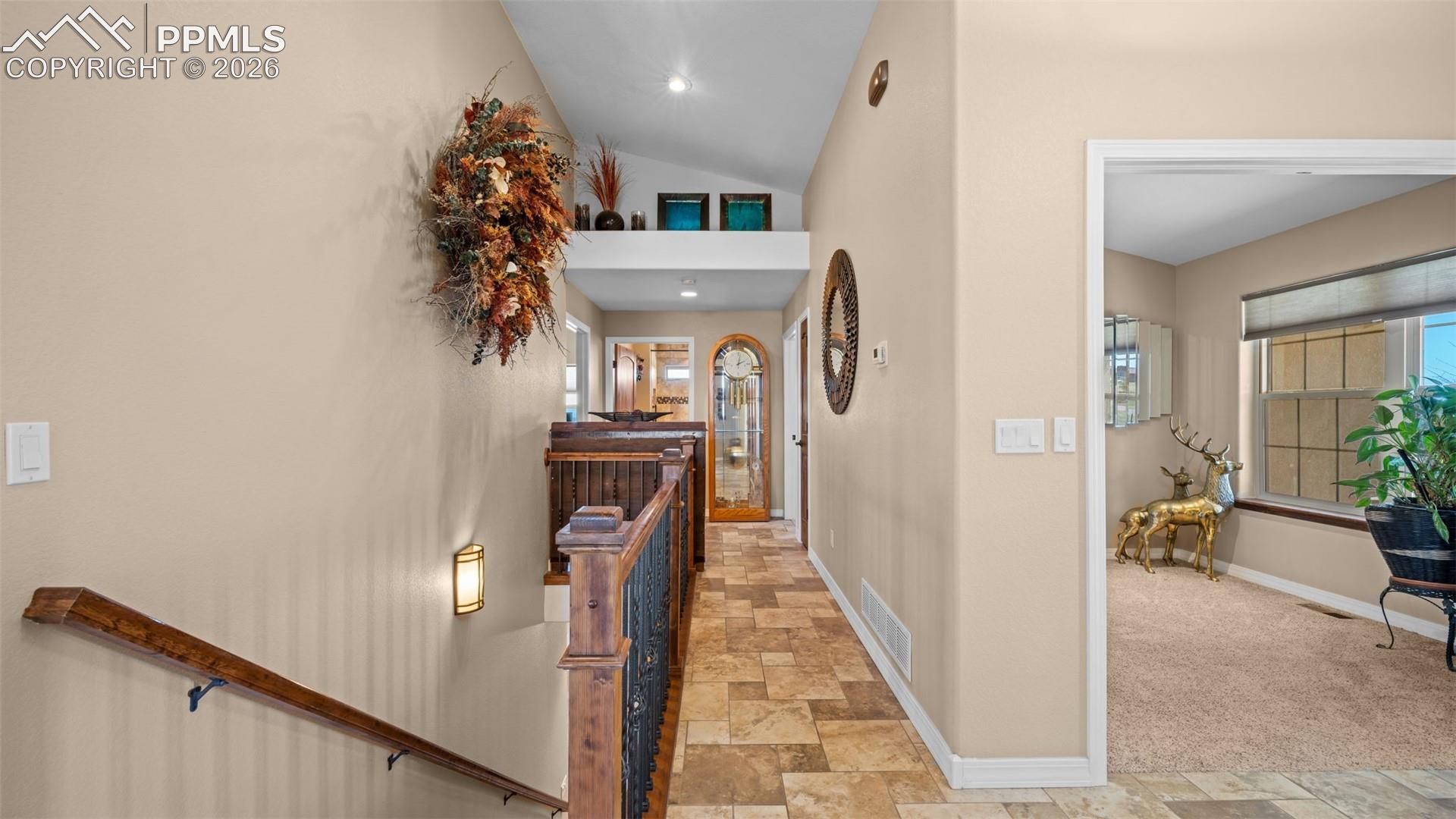 Corridor featuring stone finish floors, lofted ceiling, and an upstairs landing