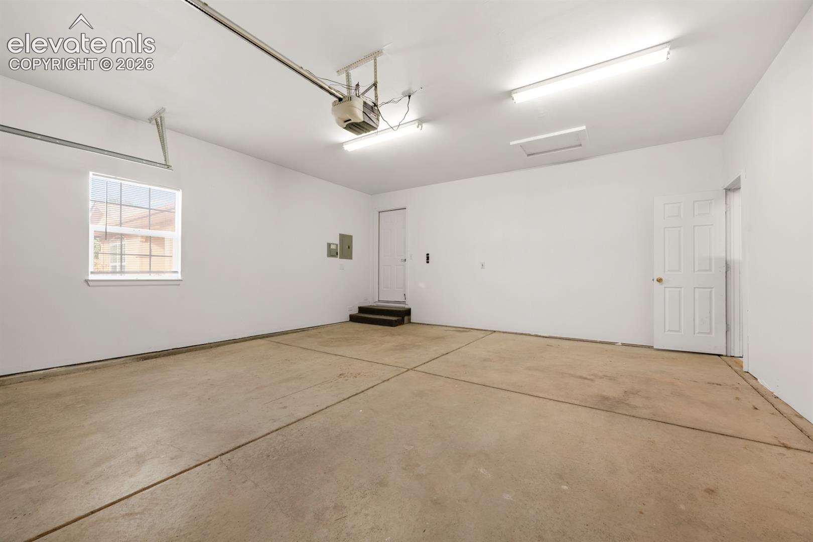 Garage space featuring finished walls, concrete flooring, dual overhead fluorescent light fixtures, and a single-hung window