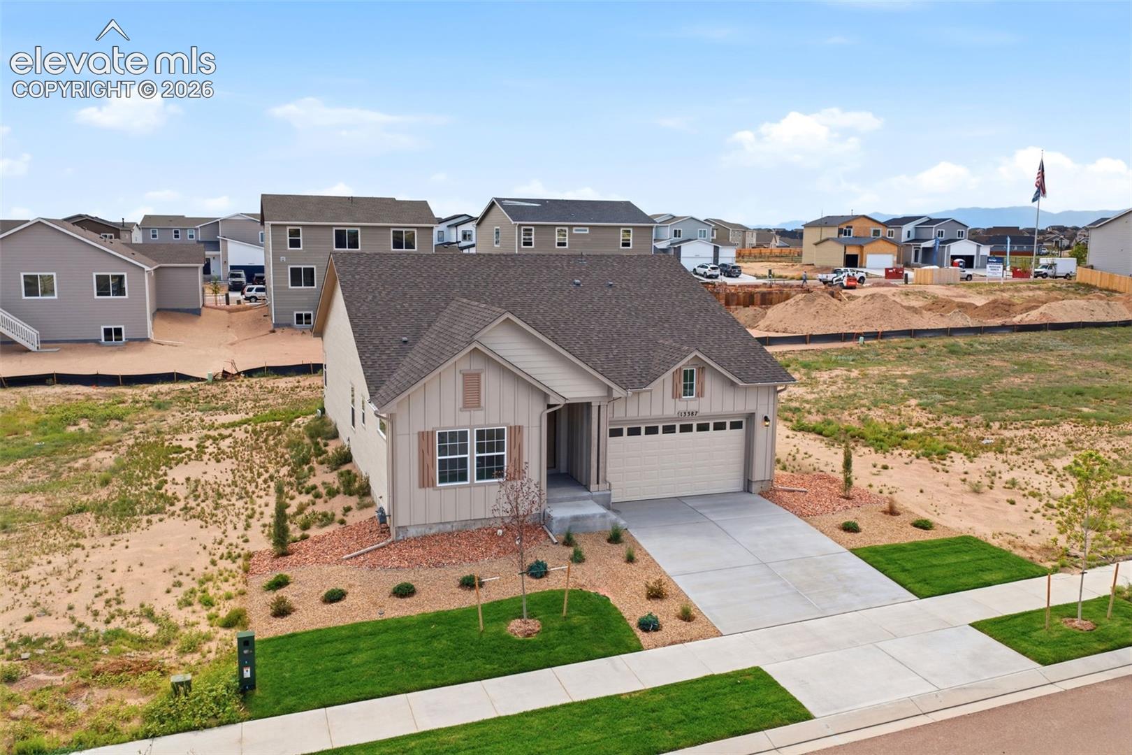 Single-story residence with vertical siding, attached two-car garage, asphalt shingle roof, concrete driveway, and xeriscaped front landscaping