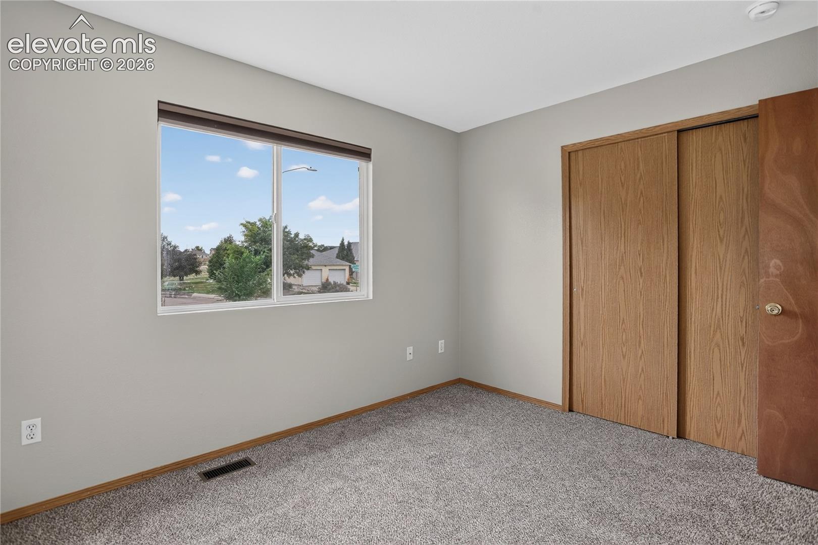 Carpeted flooring, window with blinds, sliding closet doors with wood-finish, and light gray wall paint