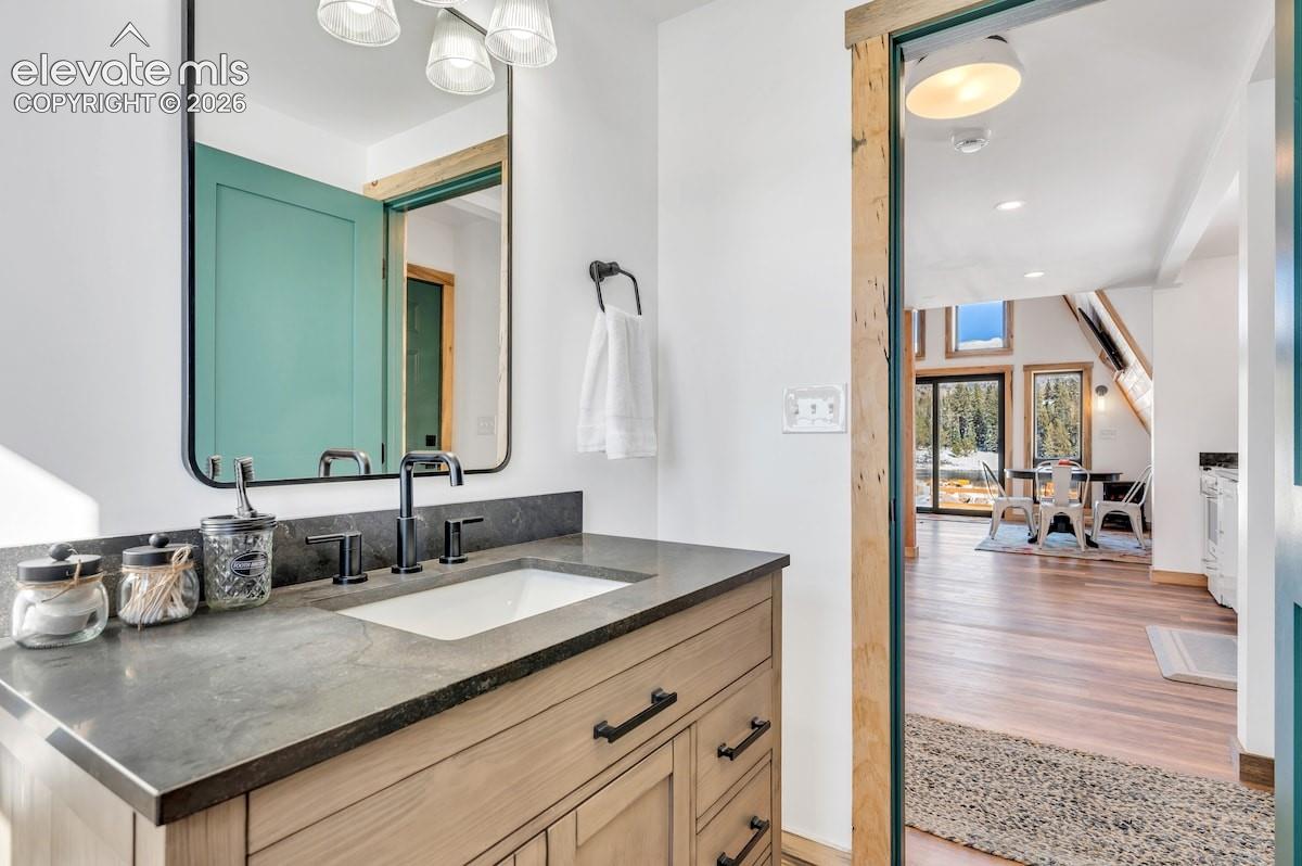 Vanity featuring a light wood-finish cabinet, dark stone countertop, undermount sink, matte black widespread faucet, and rectangular mirror