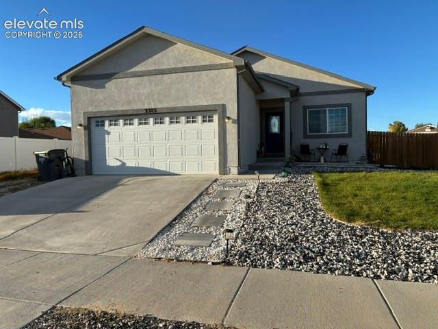 Single-story stucco exterior featuring a two-car garage, concrete driveway, stone ground cover, and a paved walkway