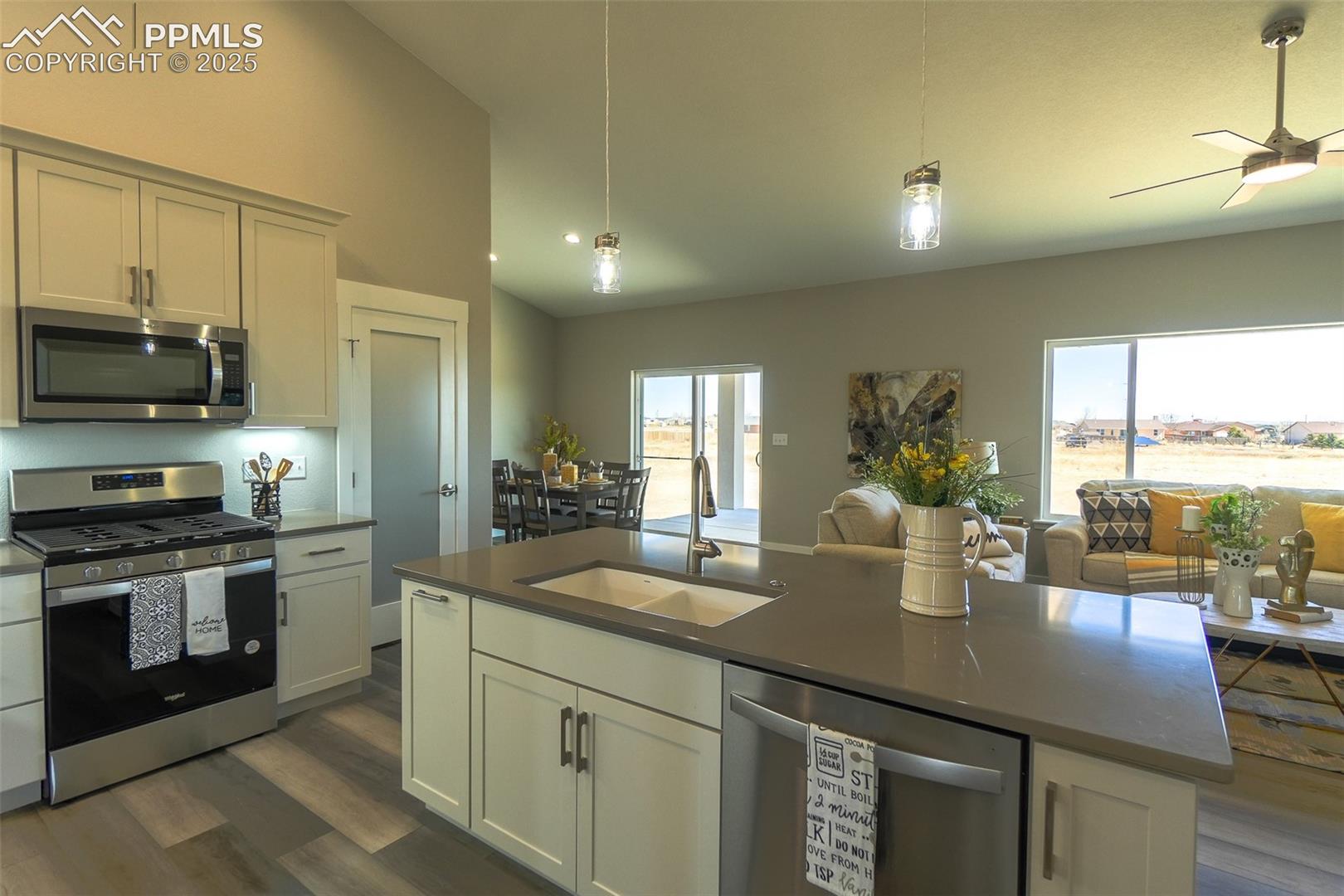 Kitchen featuring LTV / wood-style flooring, an island with sink, ceiling fan, stainless steel appliances, and sink
