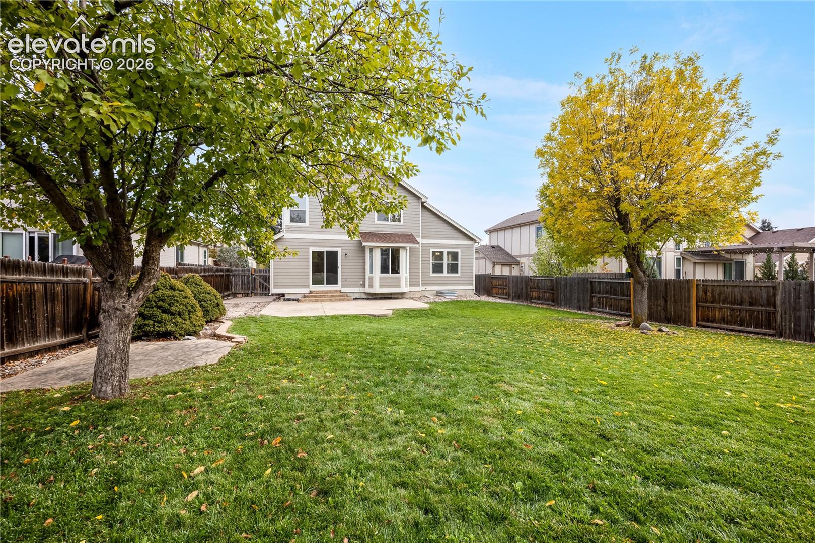 Expansive backyard featuring a concrete patio, manicured lawn, perimeter wood fencing, and mature trees