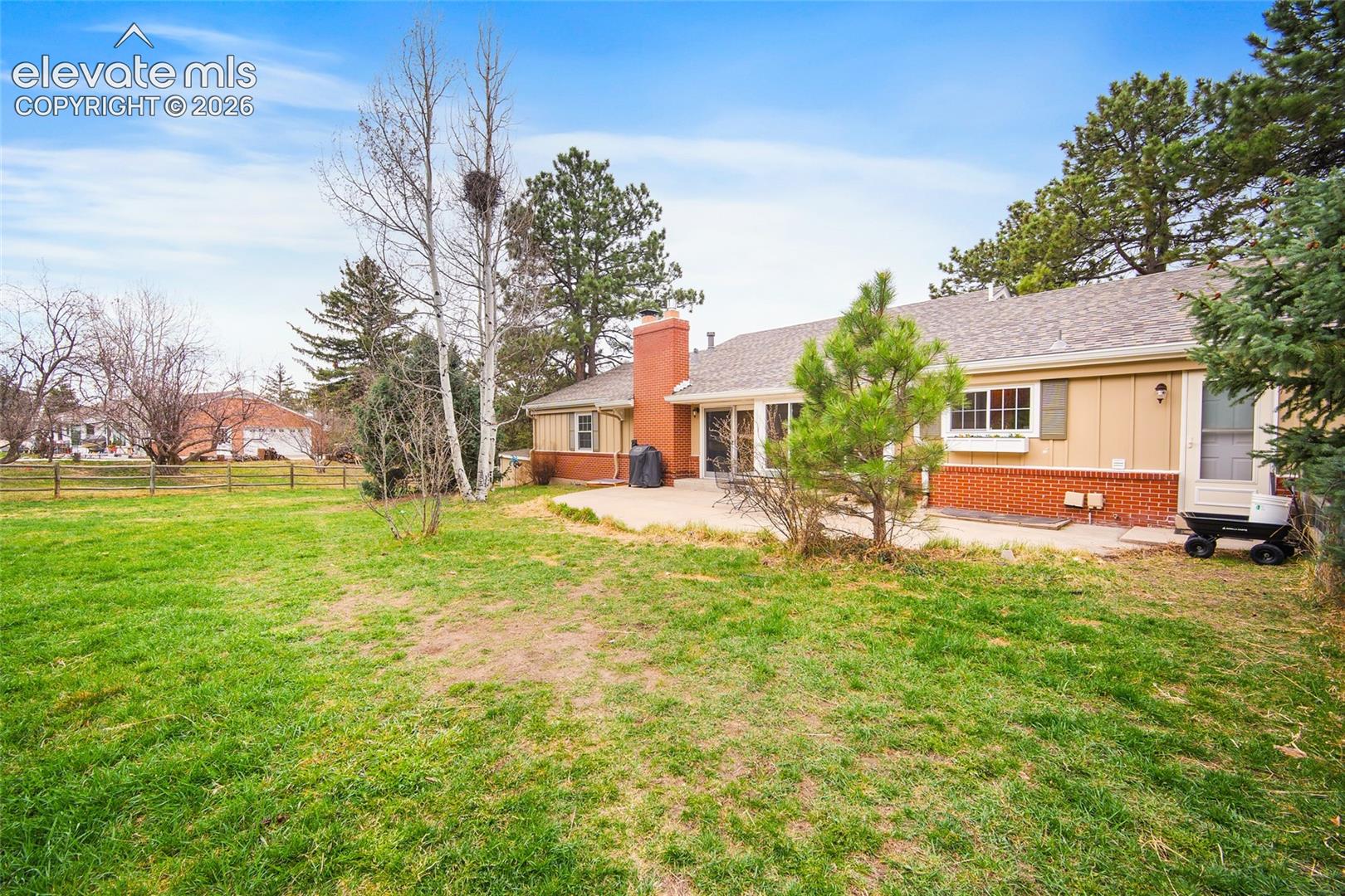 Expansive backyard featuring a level lawn, concrete patio, exterior brick masonry, and mature trees