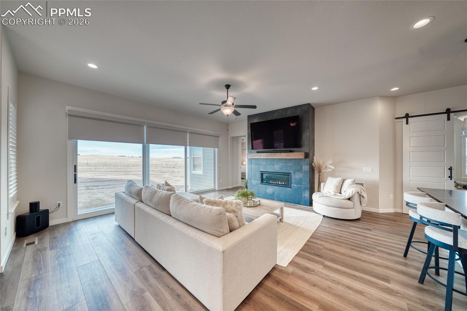 Living area featuring a barn door, light wood-style flooring, a ceiling fan, a tile fireplace, and recessed lighting