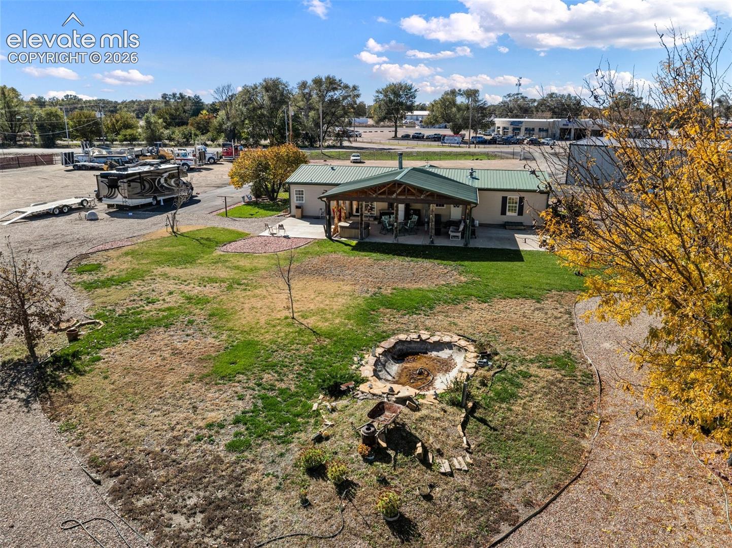Expansive grounds featuring a covered rear patio, metal roof, gravel driveway, and a stone-lined garden feature