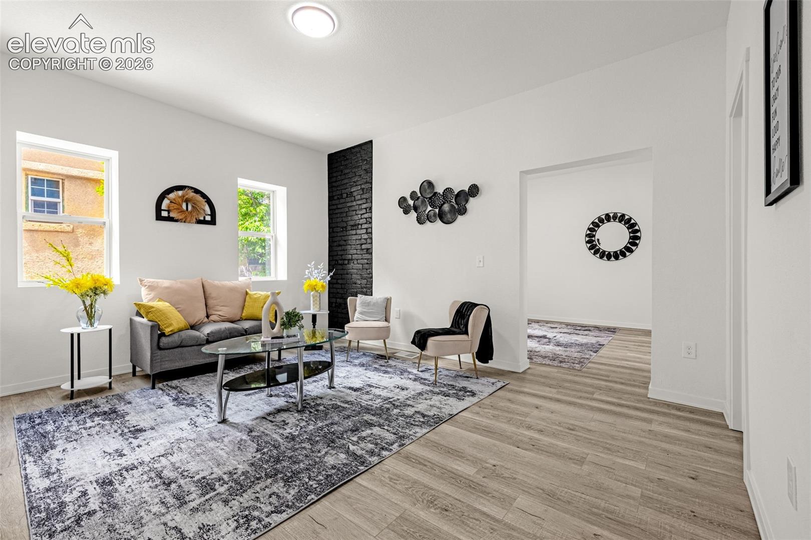 Bright living area featuring wood-finish flooring, white walls, and a prominent black brick accent wall