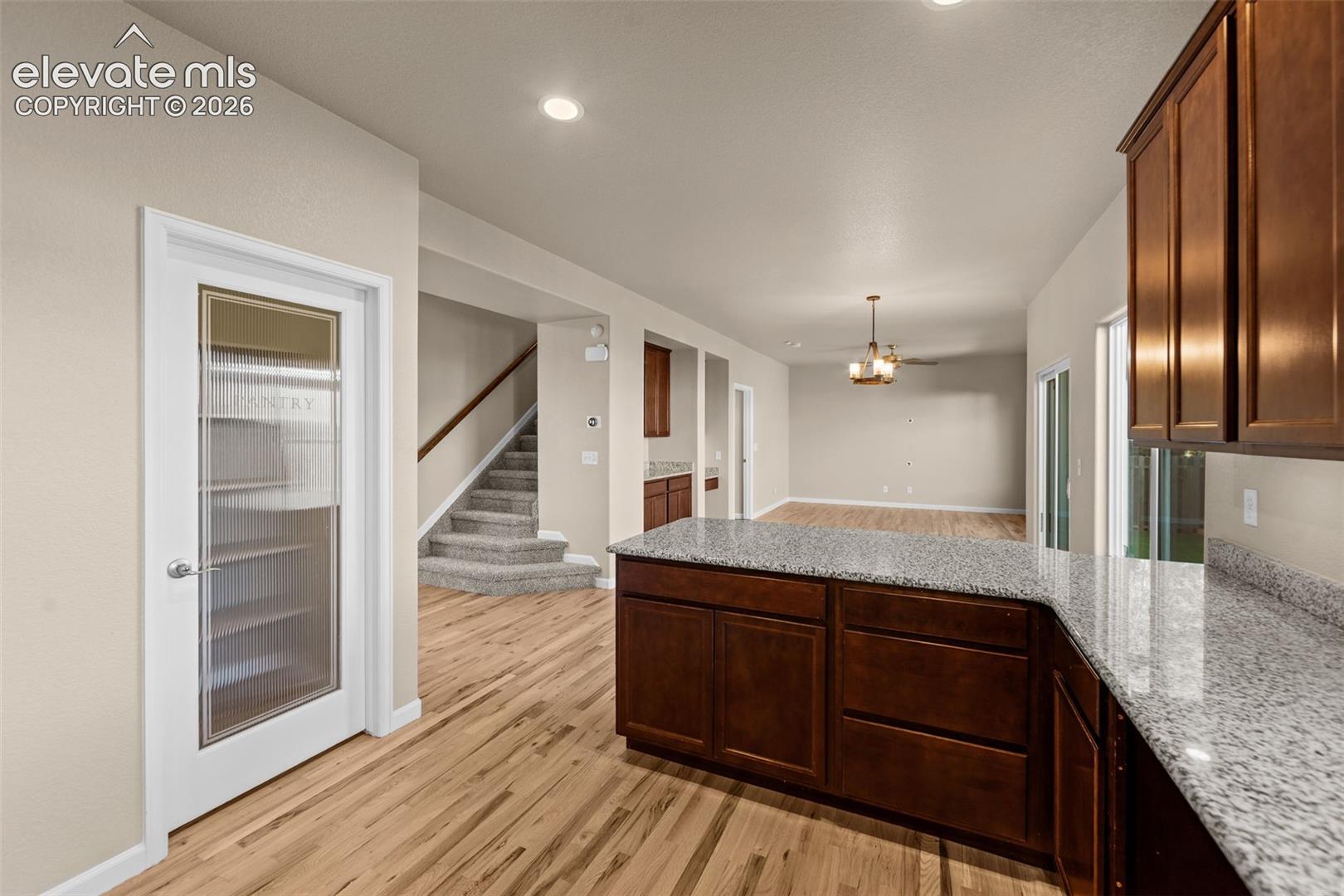Kitchen featuring wood-finish cabinetry, stone-surface countertops, wood-finish flooring, and a pantry with a glass-panel door