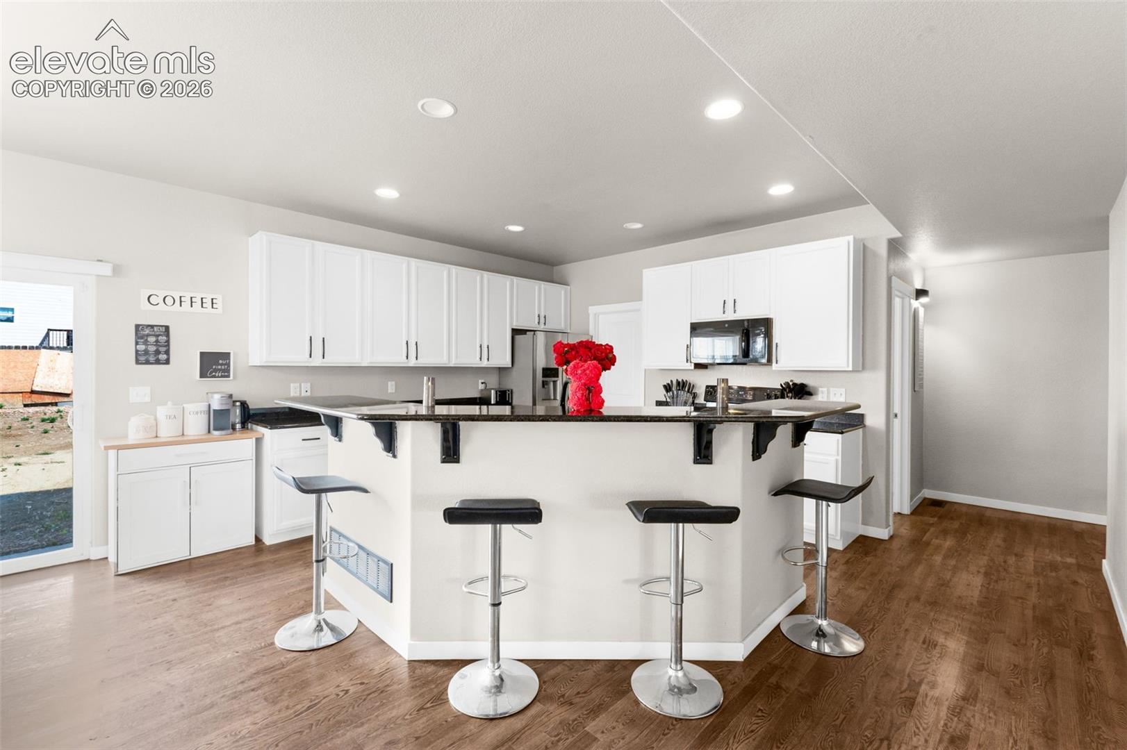 Kitchen featuring white cabinetry, dark countertops, a breakfast bar, recessed lighting, and wood-finish flooring