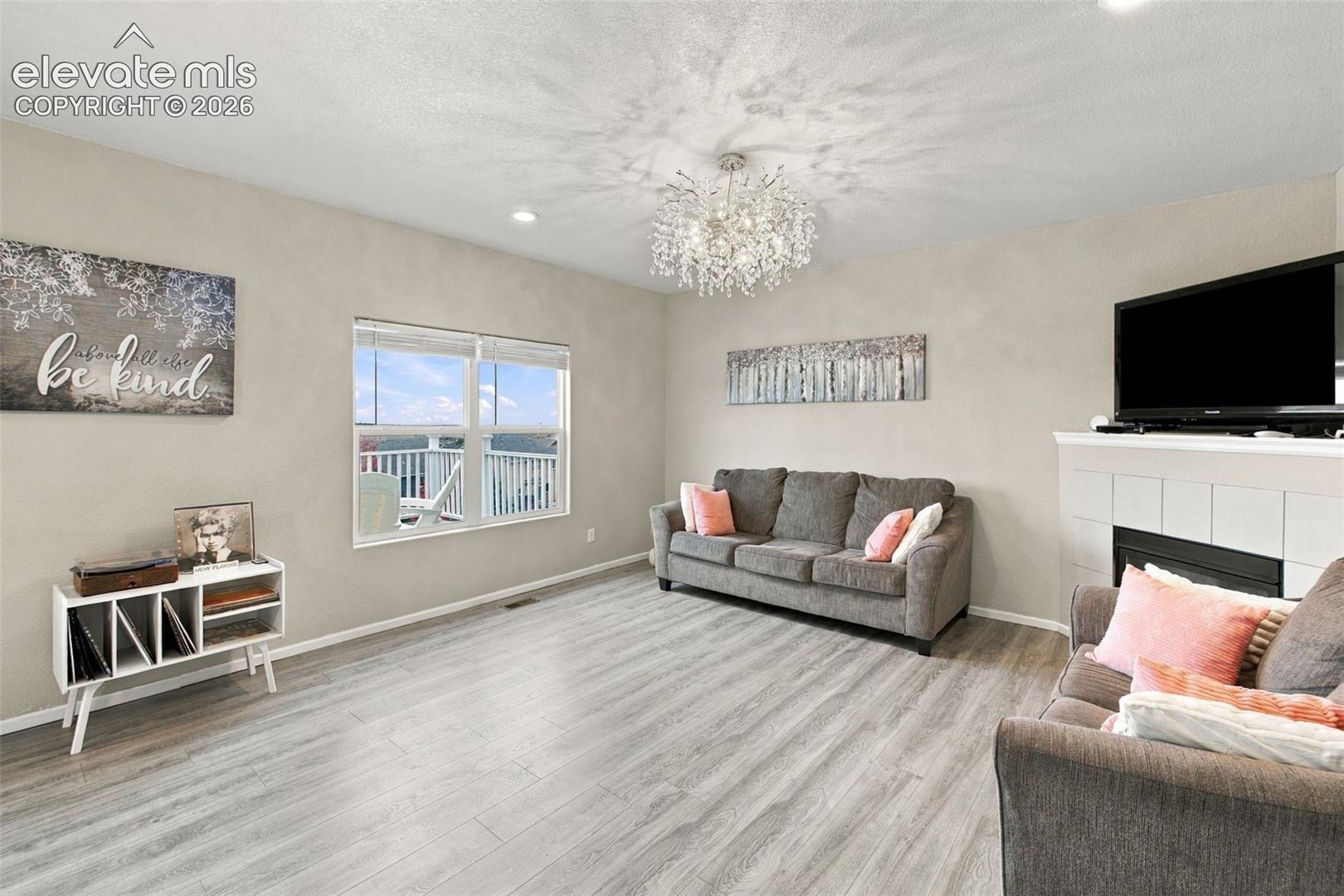 Living area featuring wood-finish flooring, a fireplace with tile surround, a crystal-style chandelier, and recessed lighting
