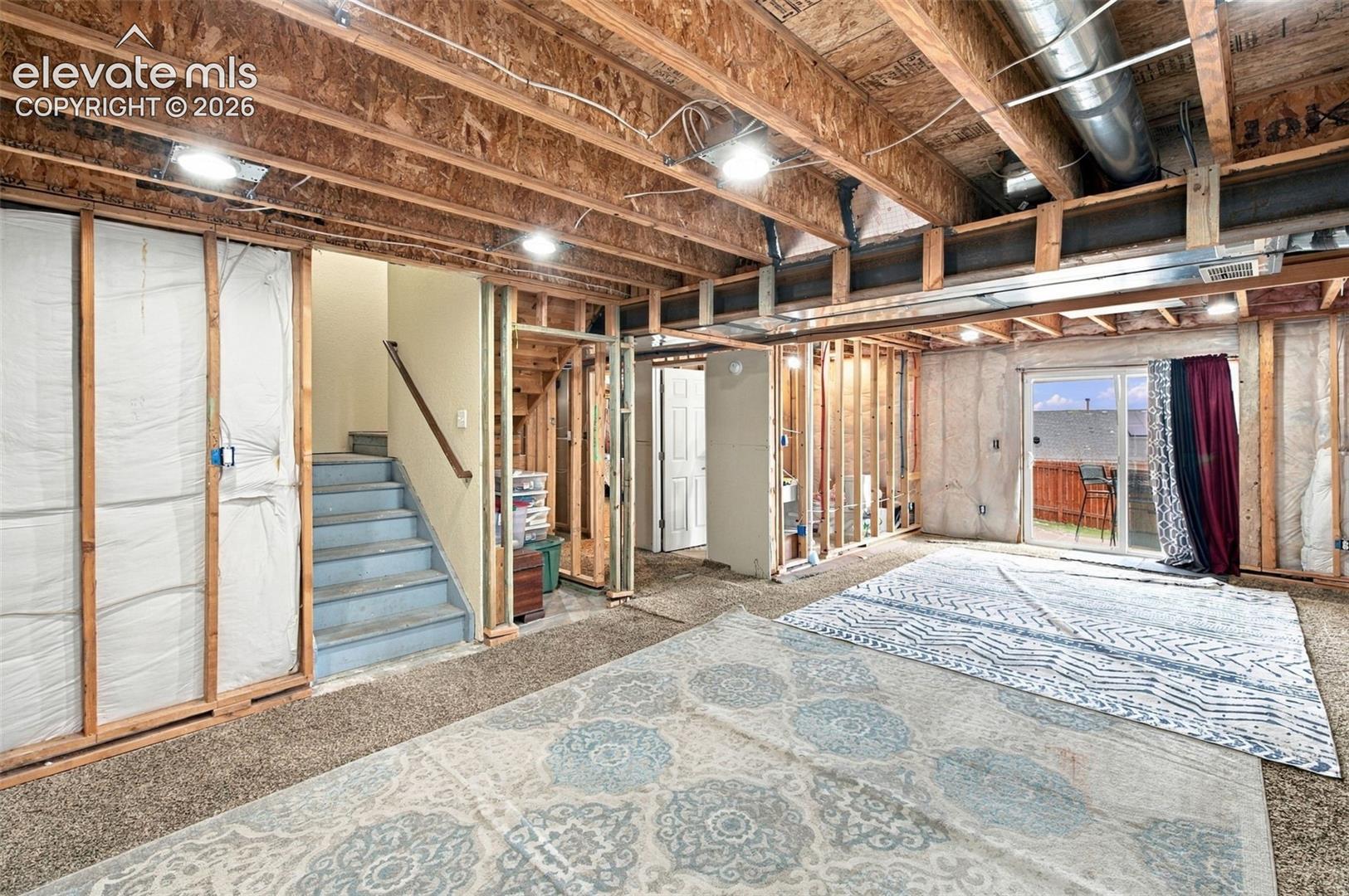 Unfinished lower level featuring exposed wood joist ceilings, recessed lighting, framed wall studs with insulation, and a sliding glass door providing exterior access