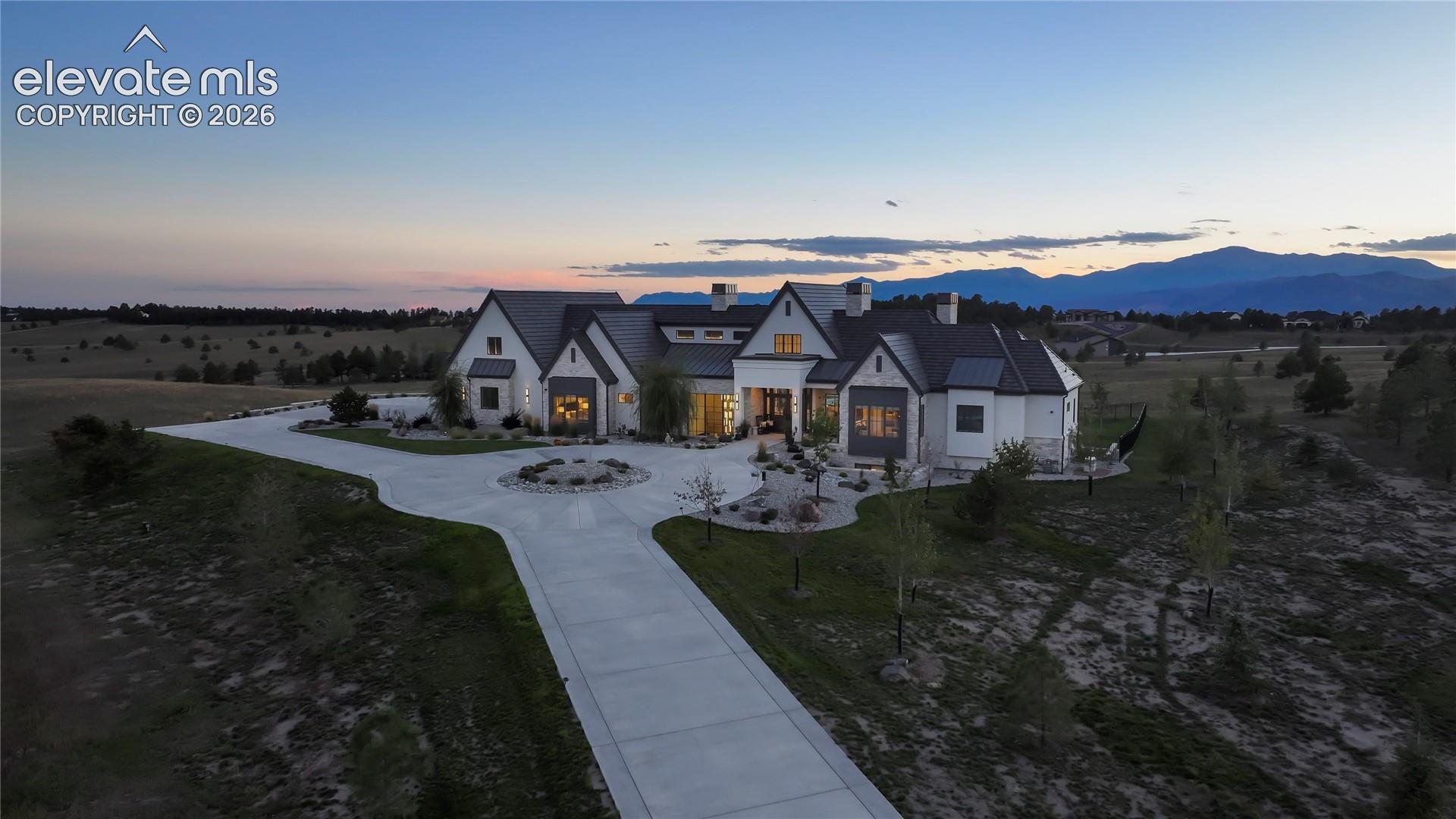 Custom multi-gabled residence featuring a stone and siding exterior, metal roof, circular concrete driveway, and mountain backdrop