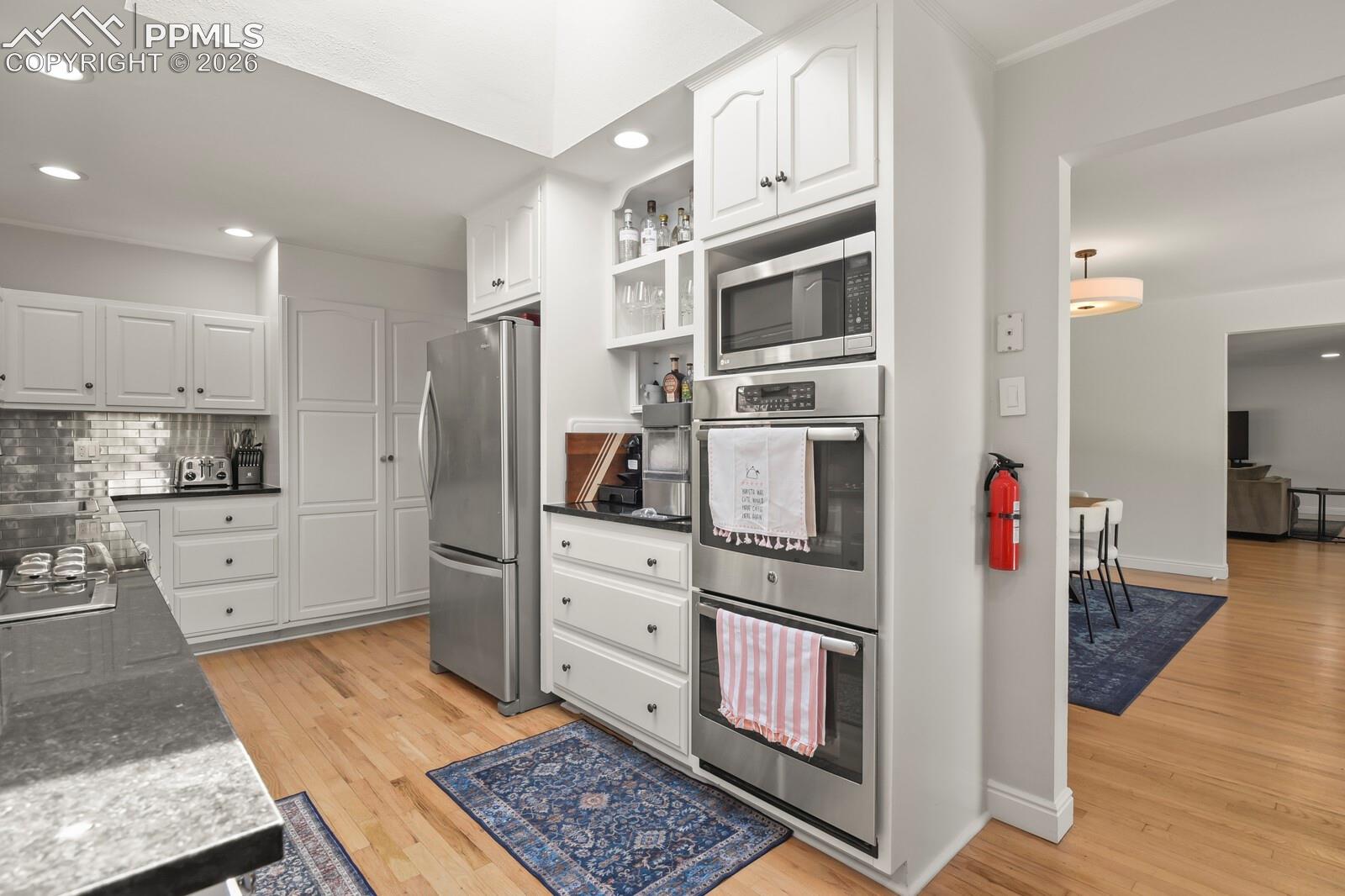 Kitchen featuring hardwood flooring, white cabinetry, stainless steel appliances, double oven, quartz countertops and a subway tile backsplash