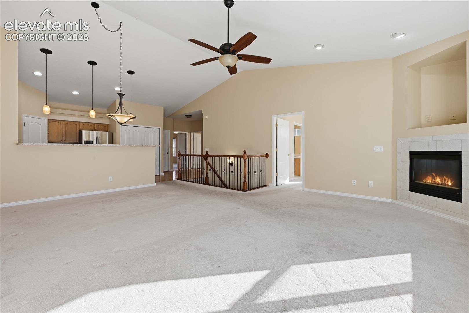 Vaulted ceilings, built-in fireplace with a tile surround, recessed lighting, ceiling fan, and metal spindle railing