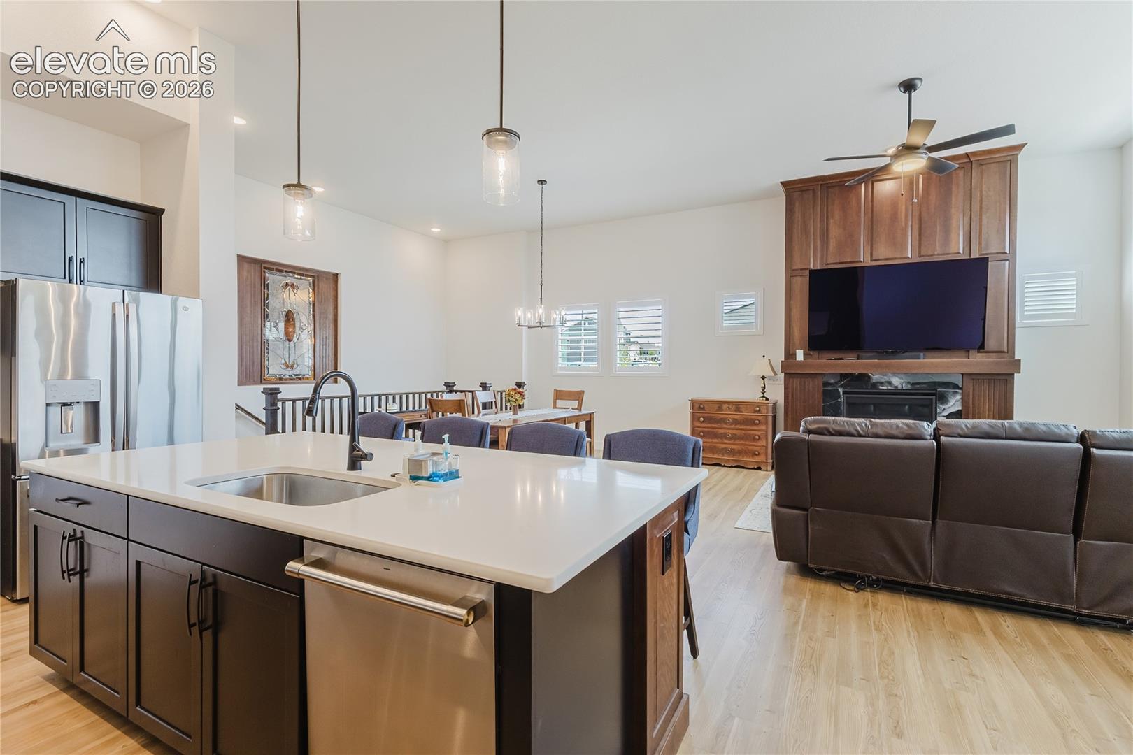 Open-concept living area with a kitchen island, sink, stainless steel appliances, fireplace with wood custom designed surround