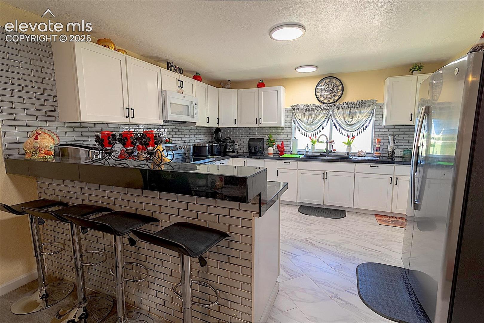 Kitchen with white microwave, freestanding refrigerator, light marble finish flooring, a peninsula, and a sink