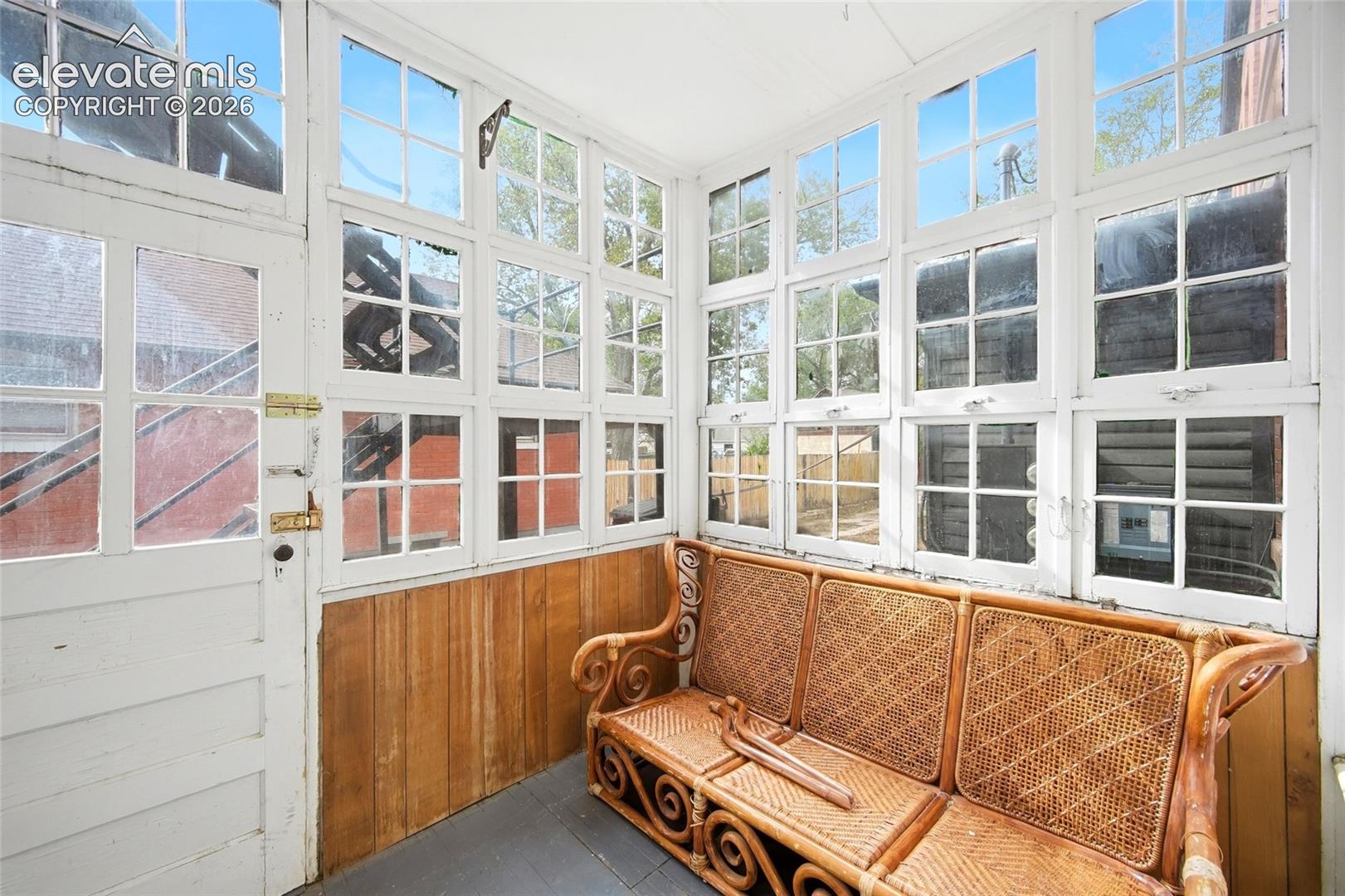 Enclosed sunroom featuring expansive multi-pane windows, wood wall paneling, and dark-toned flooring