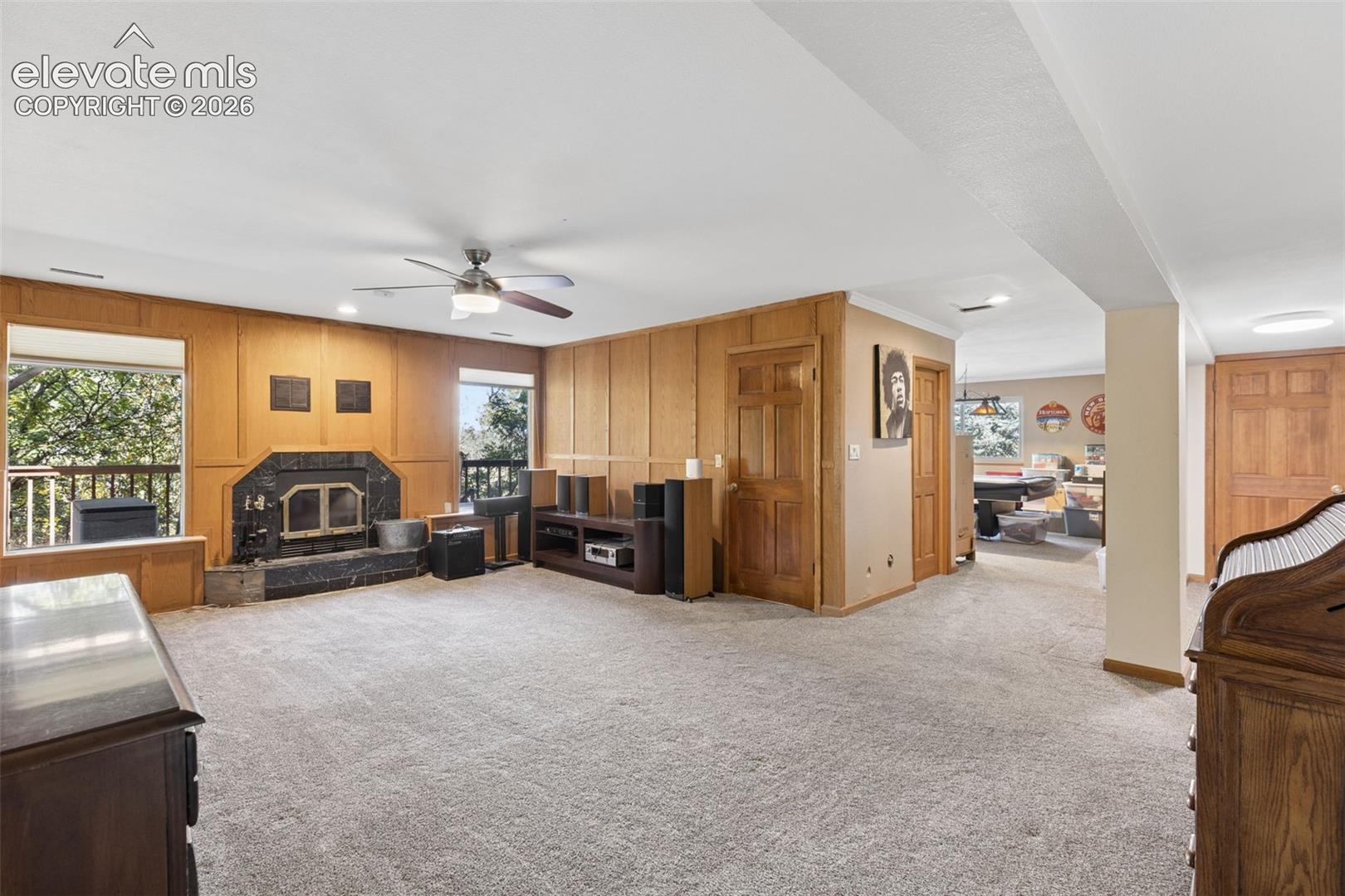 Wood paneling, stone-surround fireplace, ceiling fan, and carpeted flooring