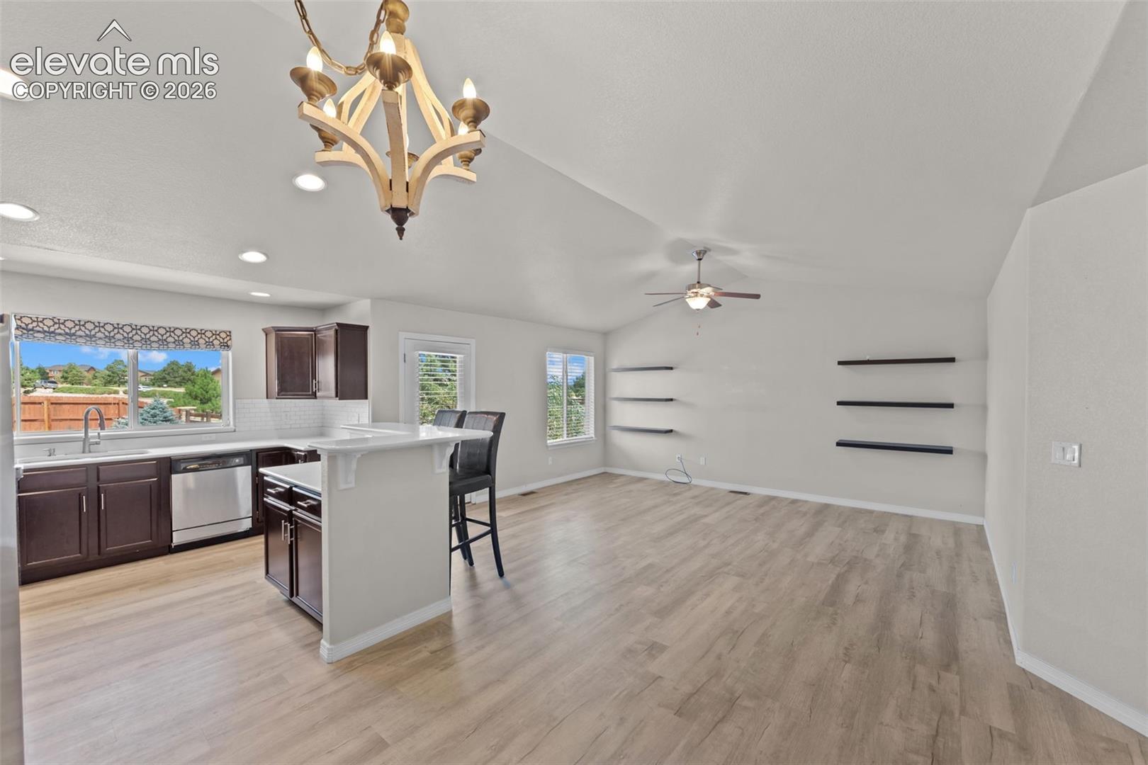 Open-concept living space featuring wood-finish flooring throughout, vaulted ceilings with recessed lighting, and a brass pendant fixture