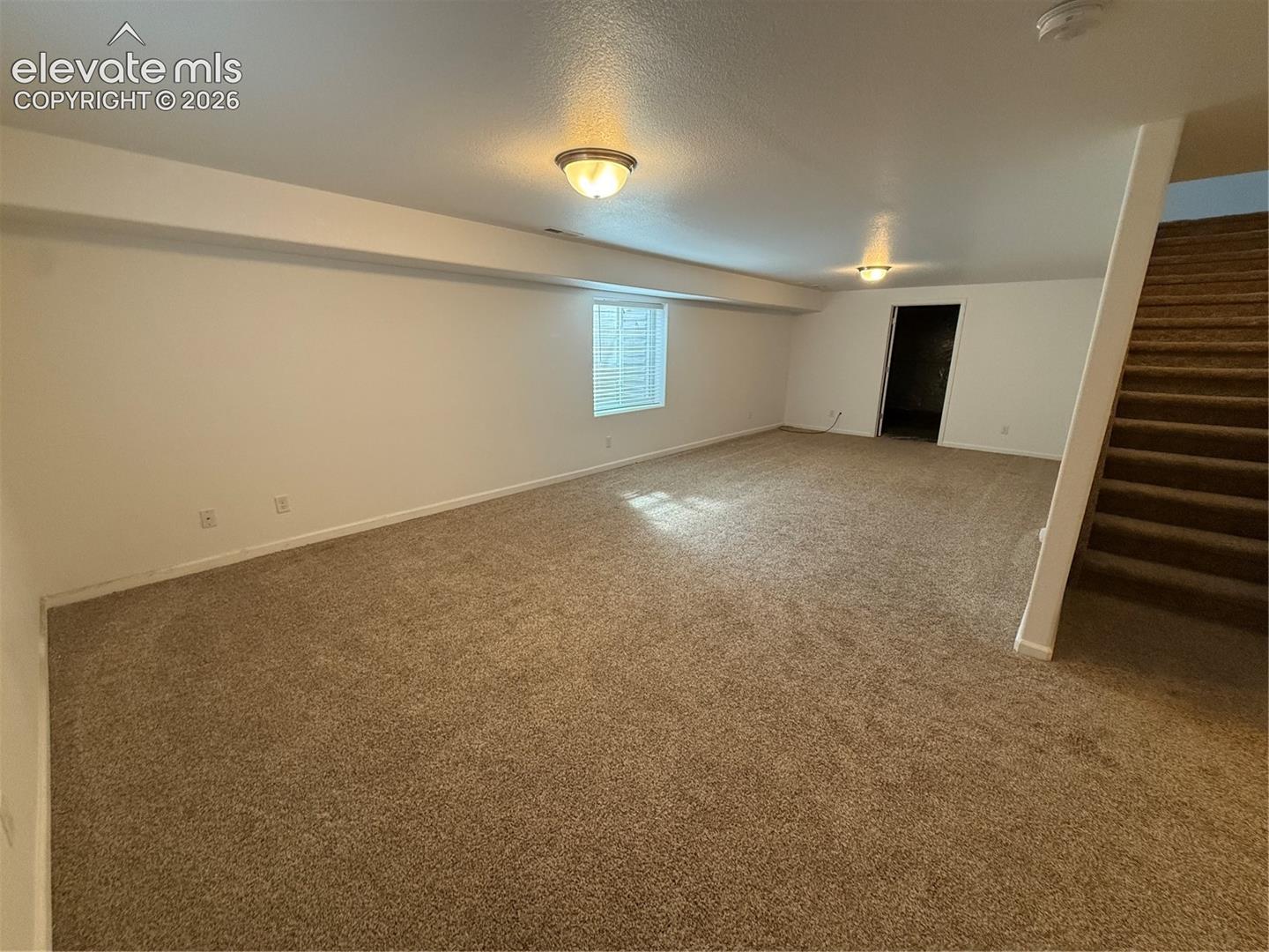Neutral-toned wall-to-wall carpeting, flush-mount ceiling lighting, single-pane window, and carpeted staircase