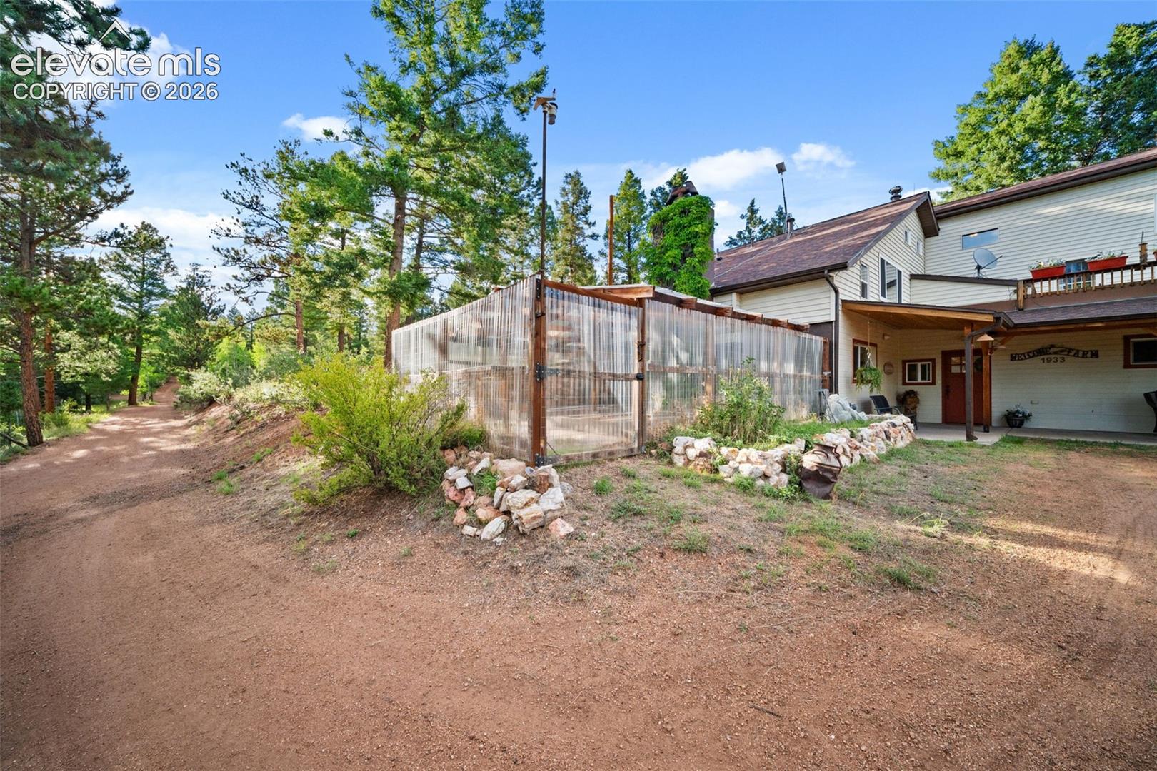 Enclosed greenhouse and garden area surrounded by mature trees.