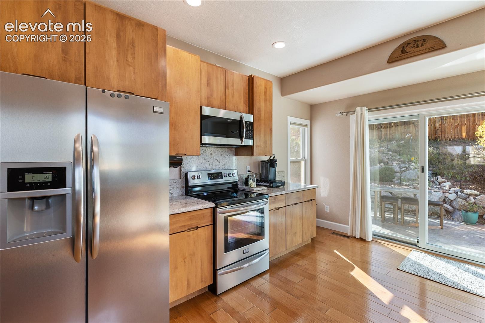 Stainless steel appliance suite, wood-finish cabinetry, light-toned countertops, wood-finish flooring, and a sliding glass door