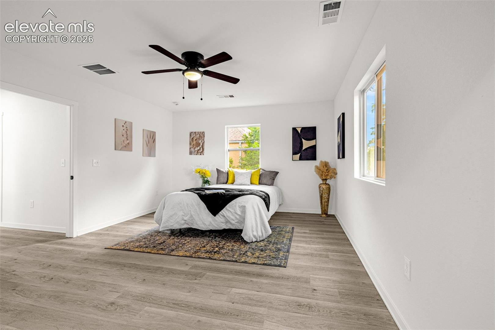 Spacious room featuring wood-finish flooring, a contemporary ceiling fan, and ample natural light from multiple windows