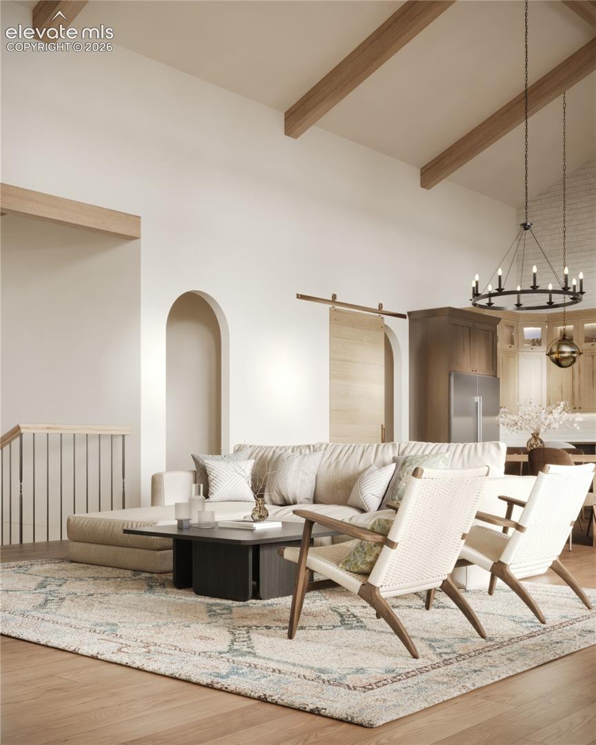 Vaulted ceiling with exposed wood beams, wood-finish flooring, arched wall openings, barn door with track hardware, and a circular chandelier
