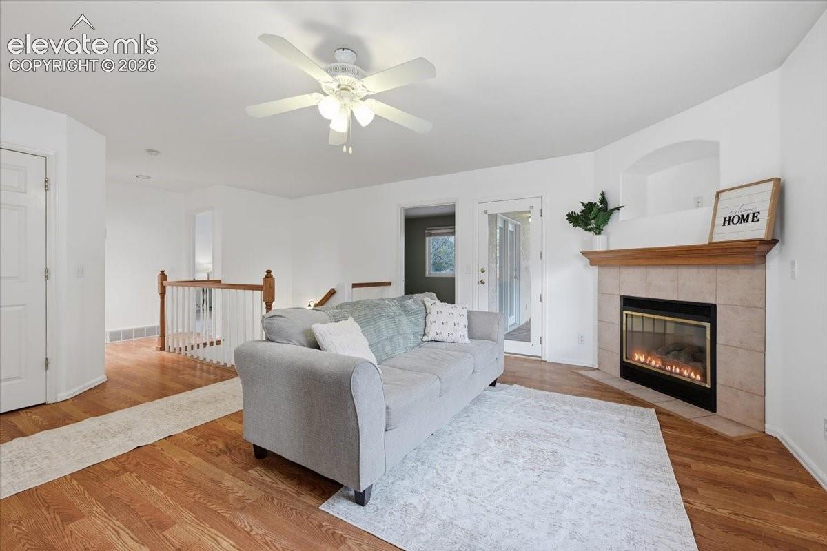 Living area featuring wood-finish flooring, a fireplace with tile surround, a built-in recessed niche, a ceiling fan, and a wood-toned mantel