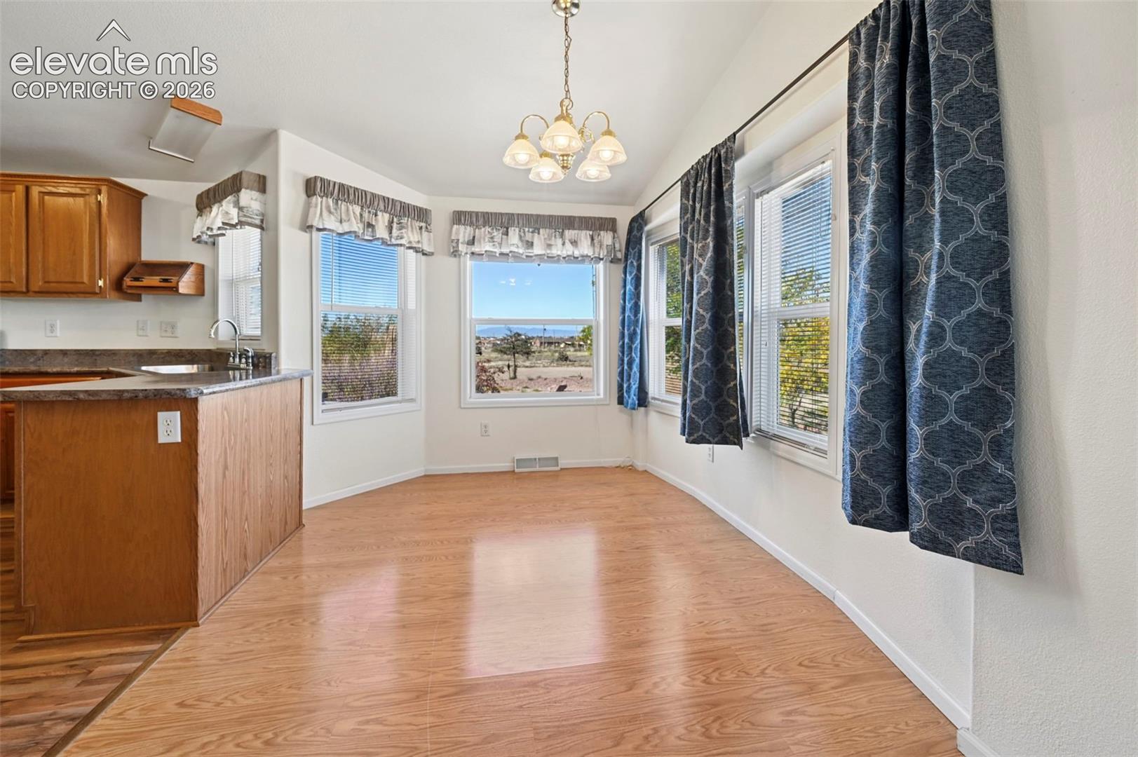Dining area featuring wood-finish flooring, a multi-arm chandelier, multiple windows with a mountain backdrop, and a kitchen peninsula with cabinetry