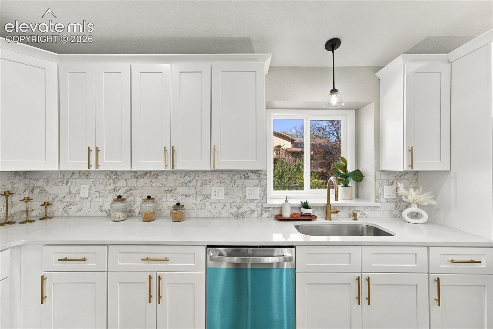 Kitchen featuring white Shaker-style cabinetry, gold-tone hardware, a solid-surface countertop, patterned tile backsplash, and an undermount stainless steel sink with a high-arch faucet