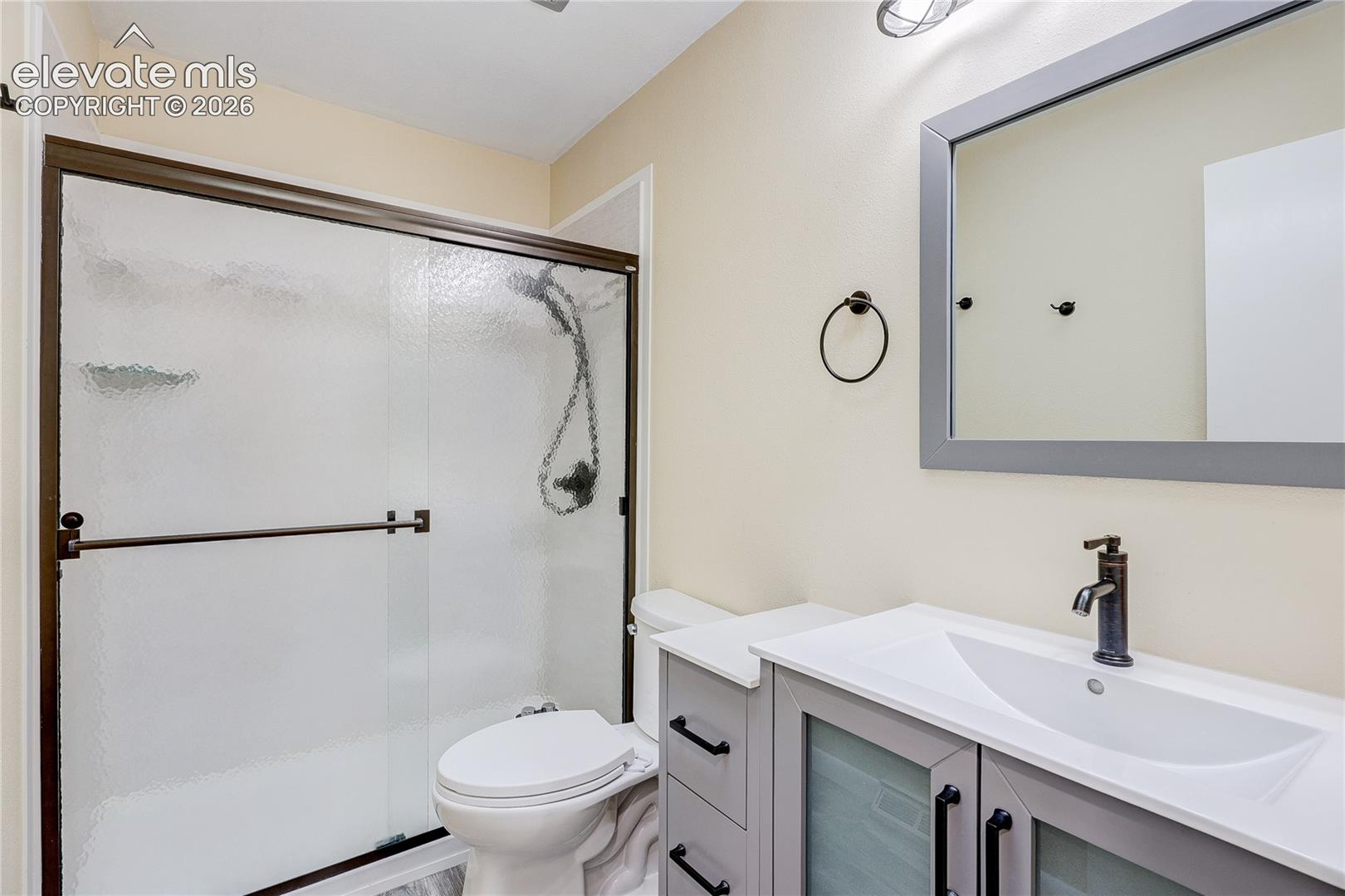 Bathroom featuring a vanity with a white countertop, inset sink, and dark hardware, paired with a shower enclosure featuring sliding glass doors and a dark frame, complemented by a framed mirror