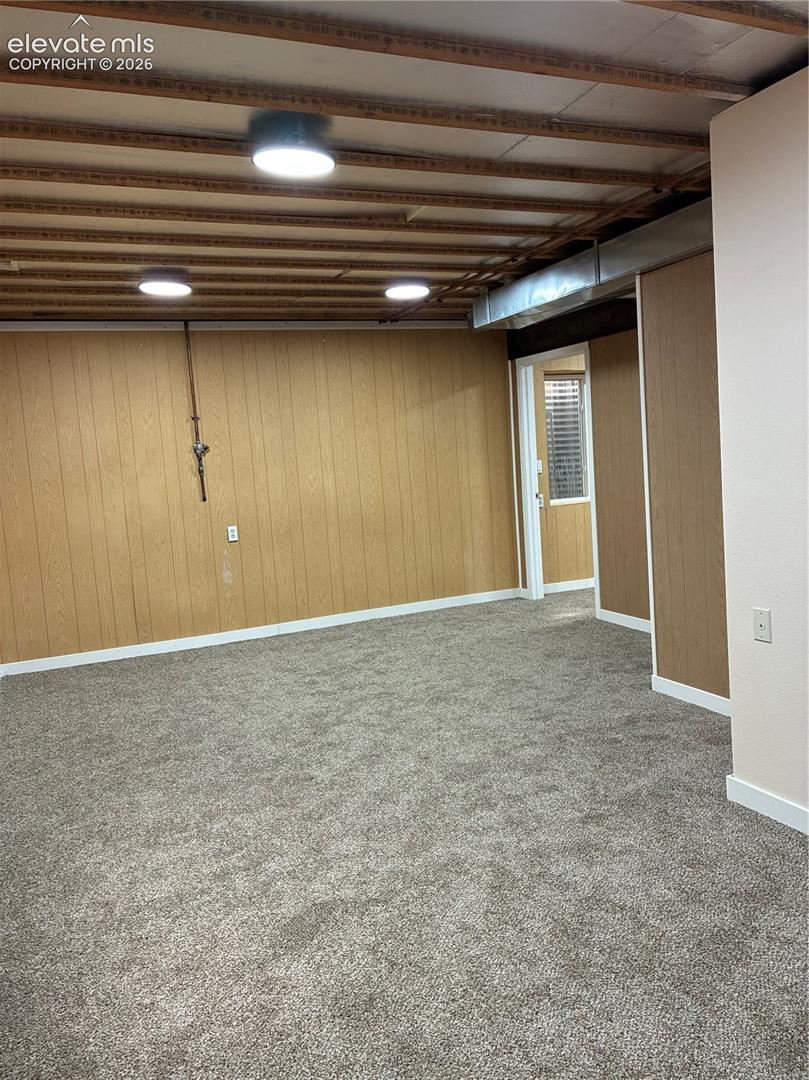 Open-concept room featuring wood-paneled walls, neutral carpeting, exposed ceiling joists, and multiple circular flush-mount light fixtures
