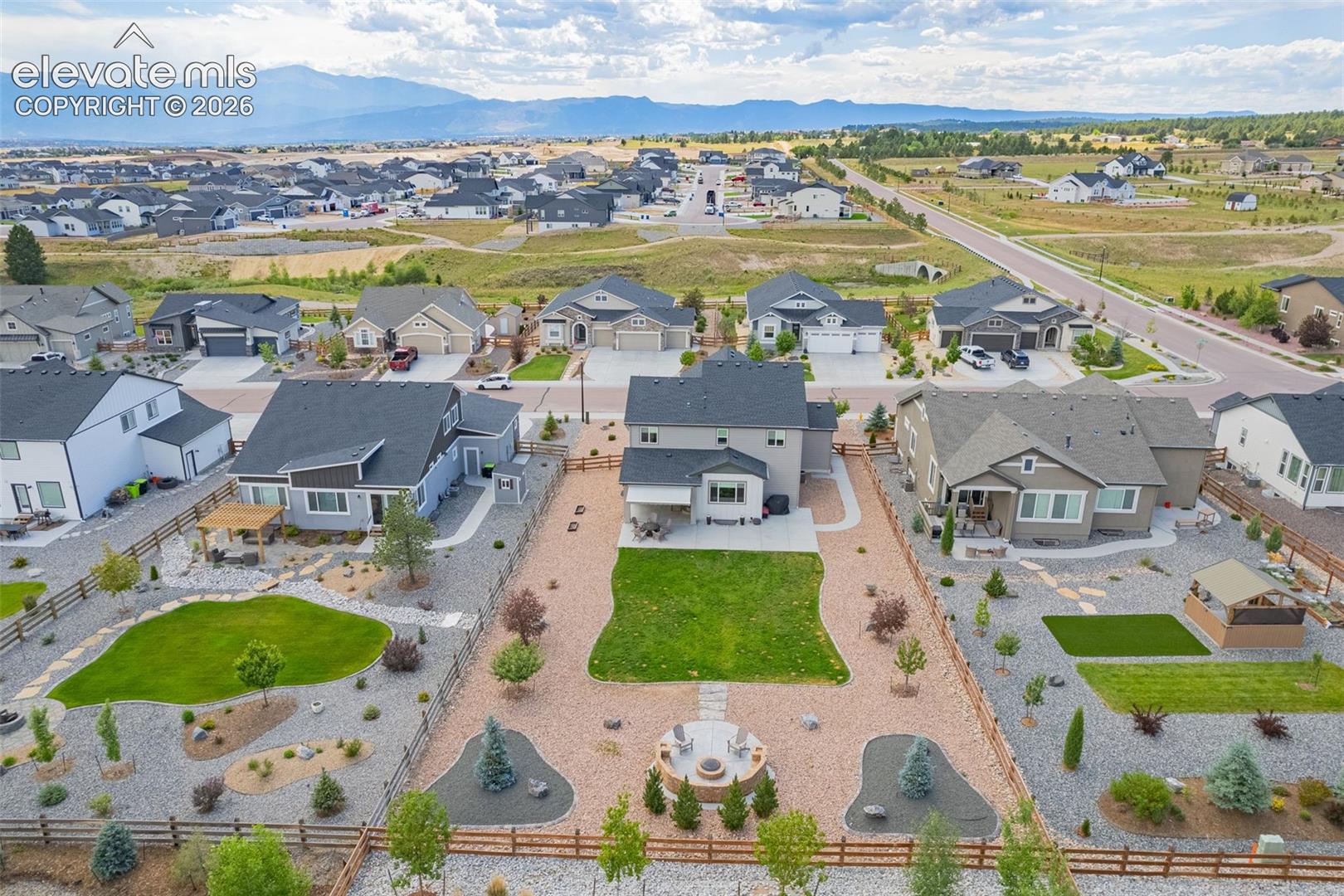 Landscaped backyard featuring a manicured lawn, gravel xeriscaping, a built-in circular fire pit, and mountain backdrop