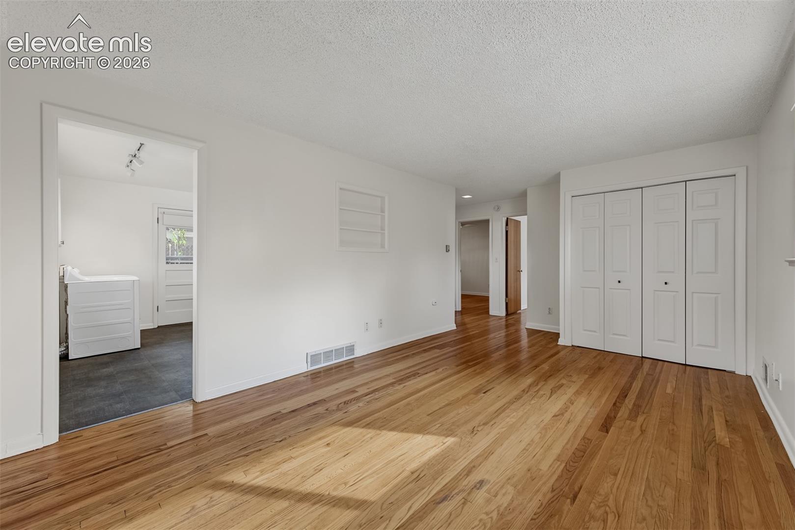 Interior space featuring wood-finish flooring, white walls, and built-in white bifold closet doors