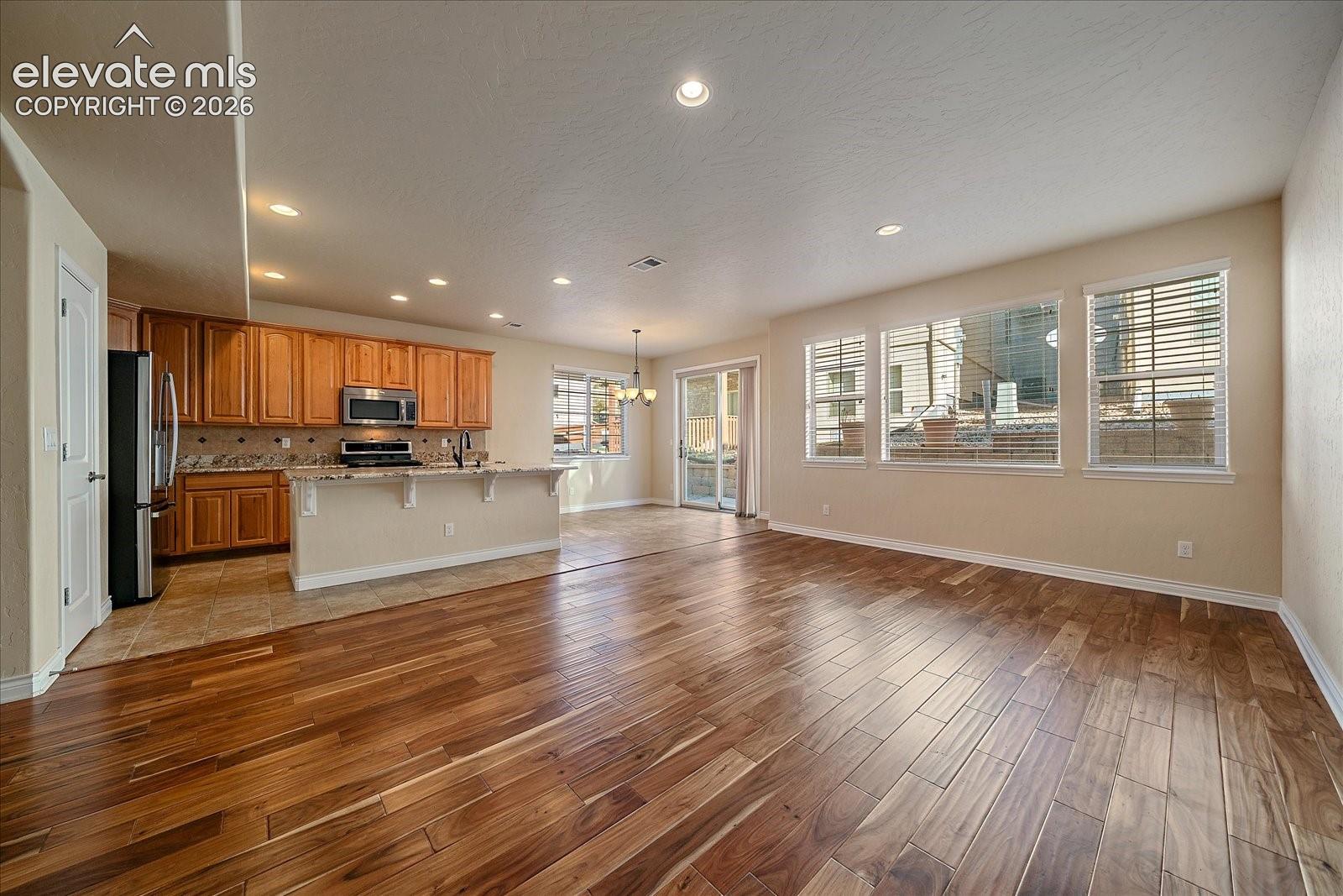 Open-concept interior featuring wood-finish flooring, recessed lighting, a kitchen with wood cabinetry and a breakfast bar, and multiple windows