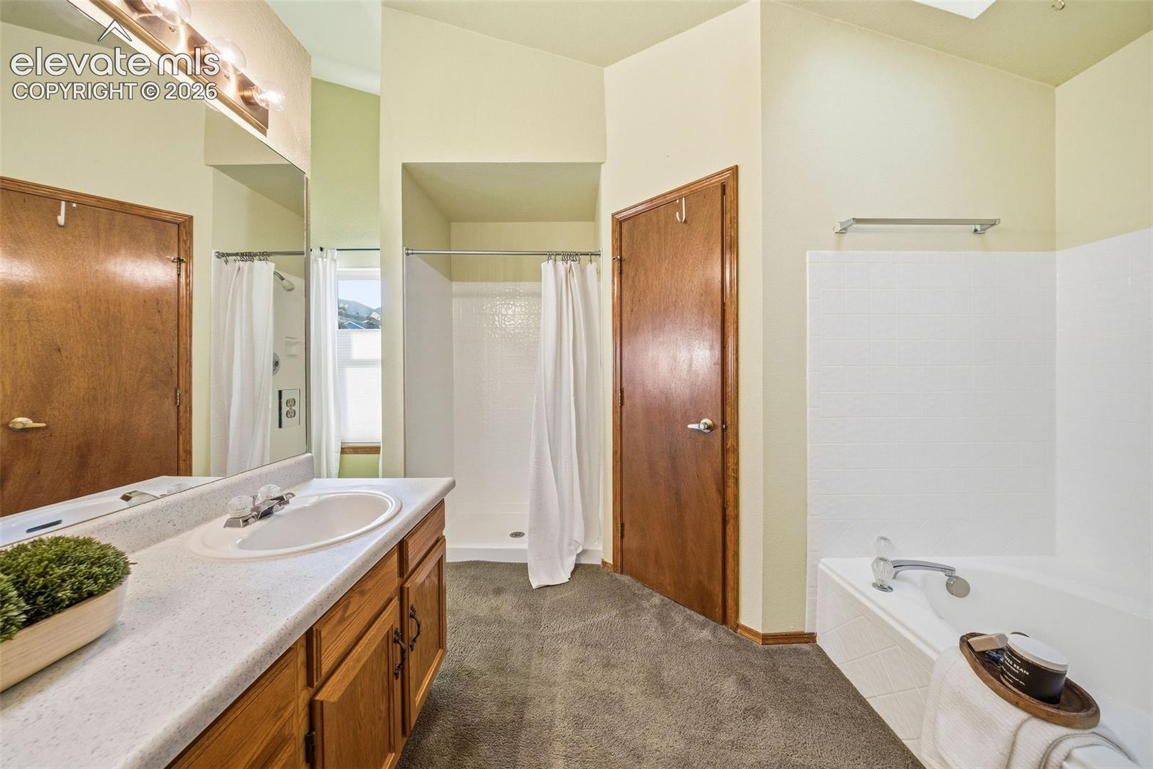 Bathroom featuring a vanity with a solid-surface countertop, an integrated sink, a built-in soaking tub with a tiled surround, a separate stall shower, and a full-width wall mirror