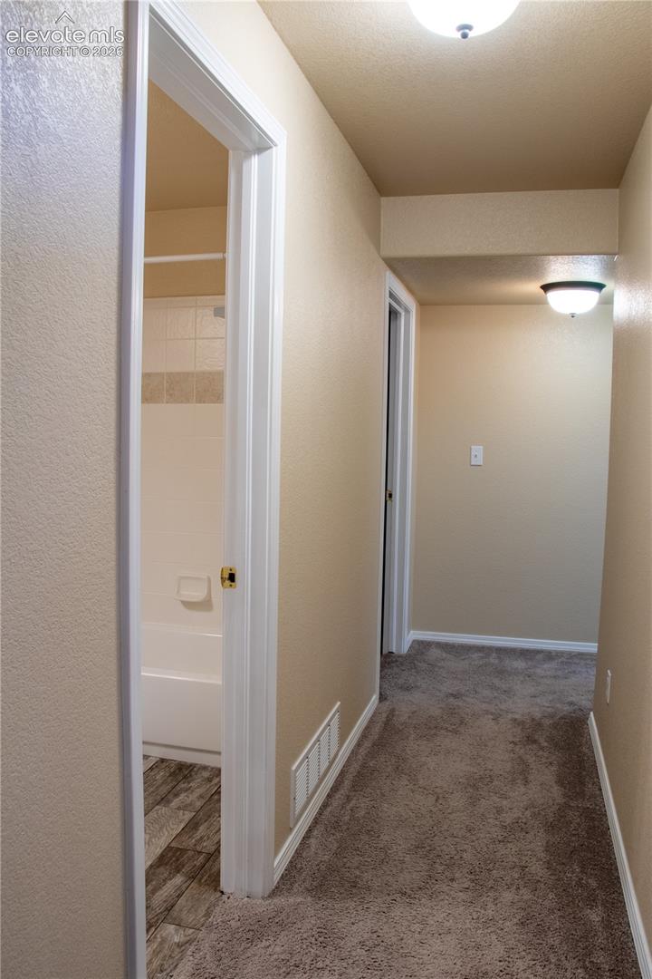 Neutral tone walls and carpeting create a cohesive corridor, illuminated by ceiling-mounted light fixtures