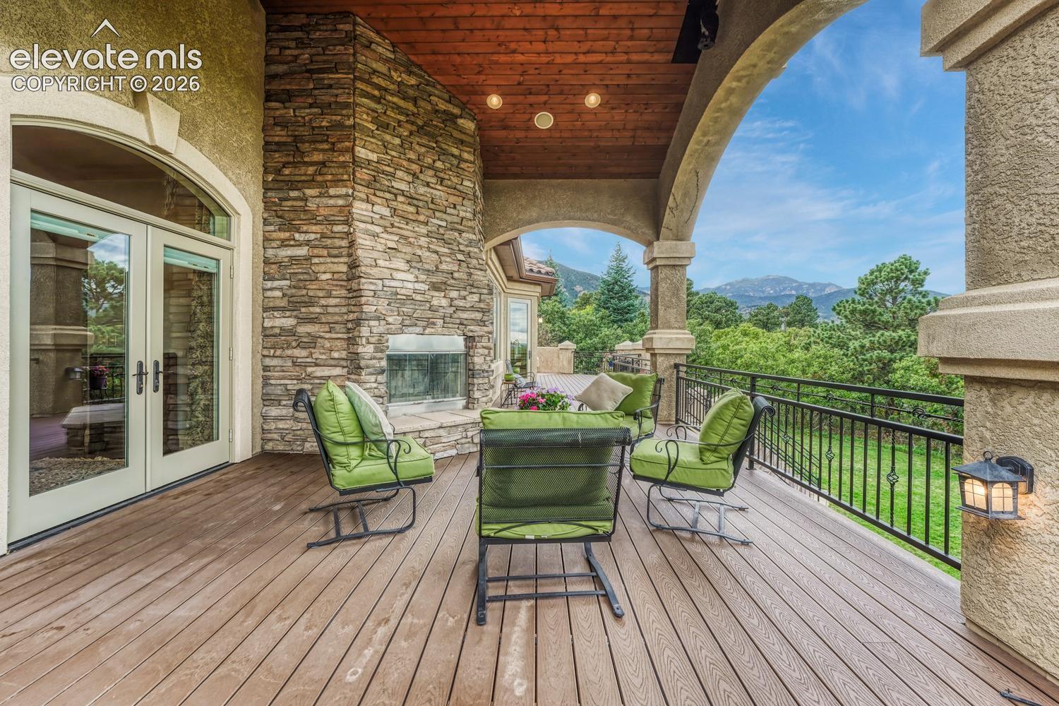 Covered patio featuring wood-finish flooring, a stacked stone fireplace, a tongue-and-groove wood ceiling, arched masonry columns, and a wrought-iron railing
