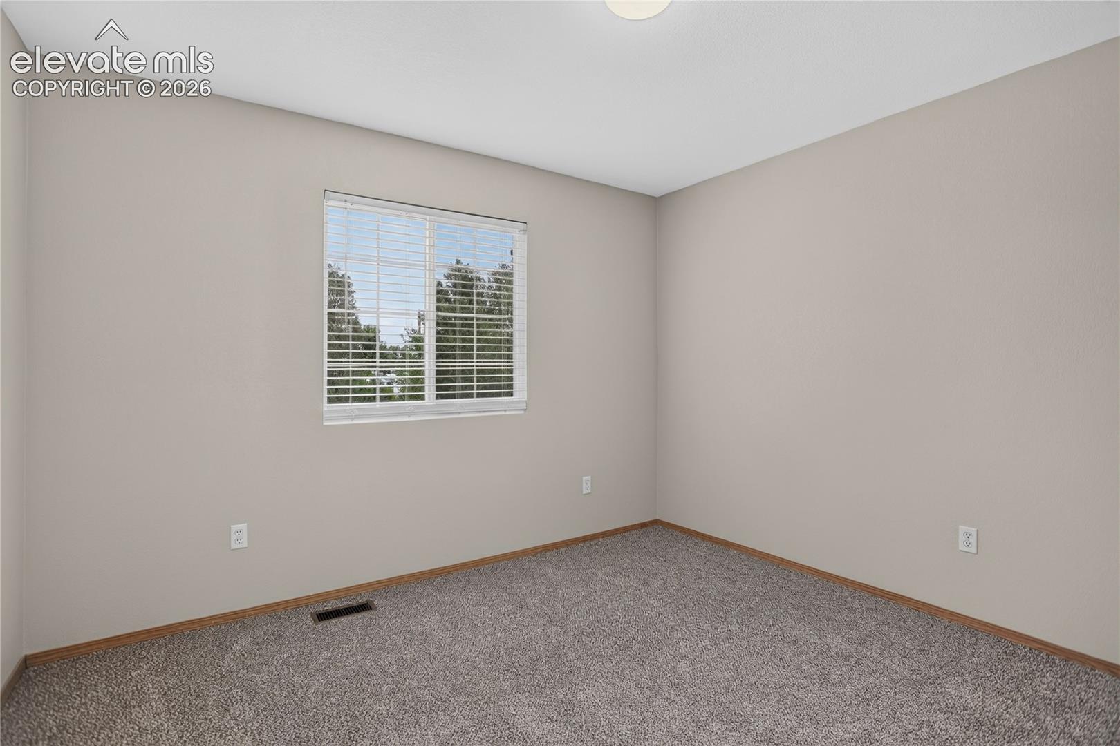 Neutral-toned walls, plush carpet flooring, window with horizontal blinds, and a flush mount ceiling light