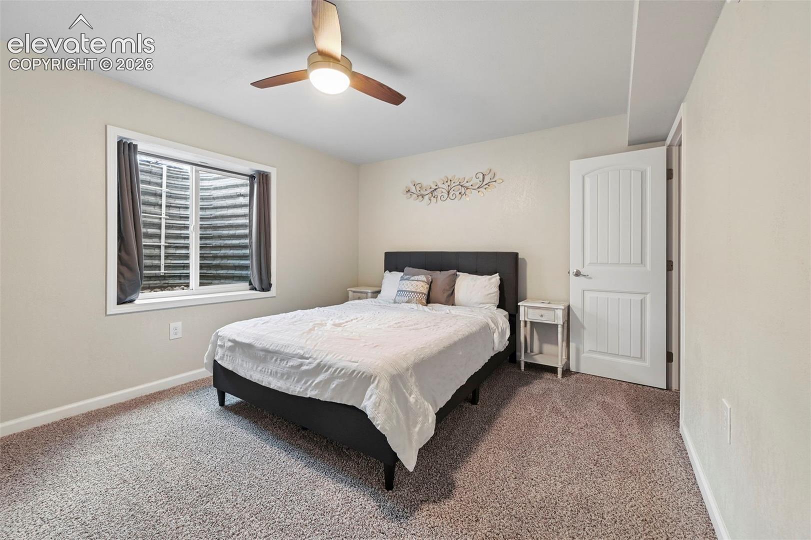 Neutral wall paint, ceiling fan with integrated lighting, window with window well, paneled interior door, and soft carpeting