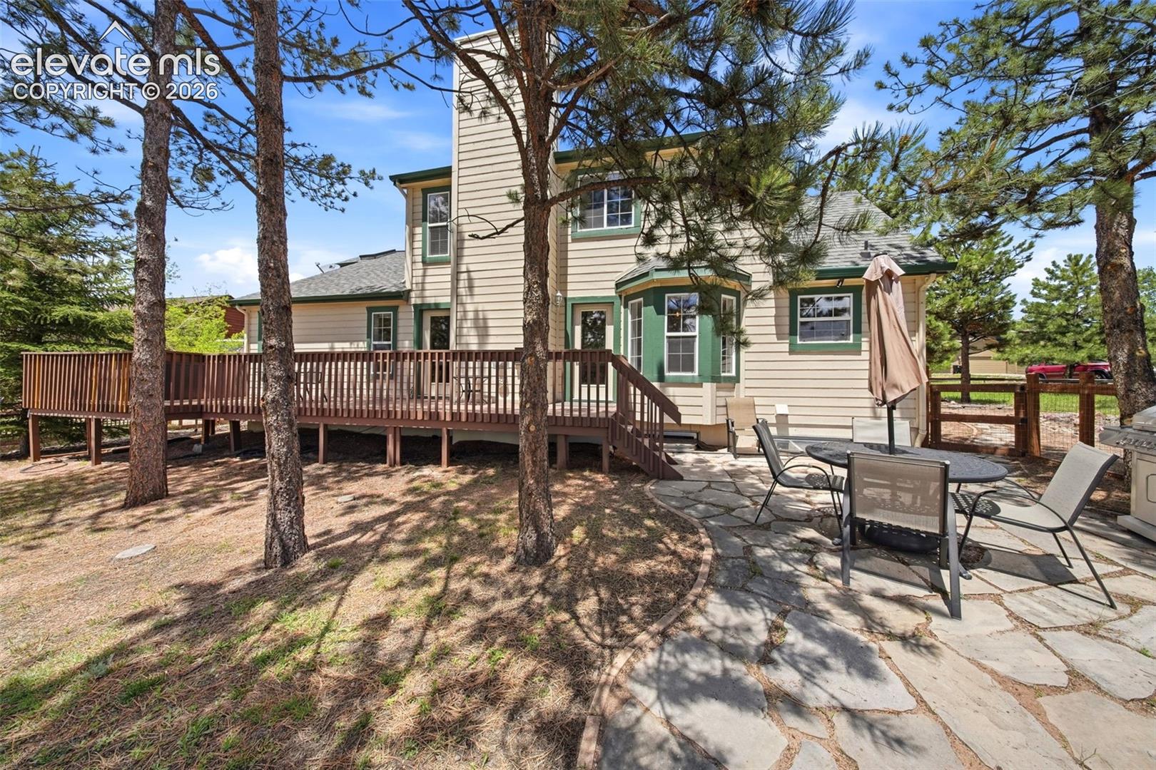 Expansive wood deck with full railing, complemented by a stone patio featuring irregular flagstone pavers