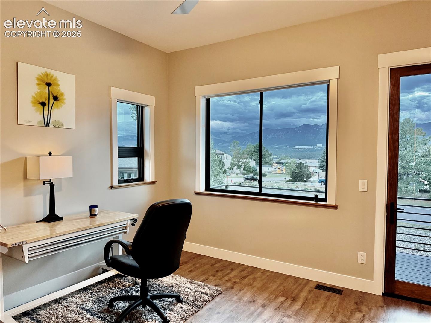 Expansive windows with mountain scenery, wood-finish flooring, light-toned wall paint, and a ceiling fan
