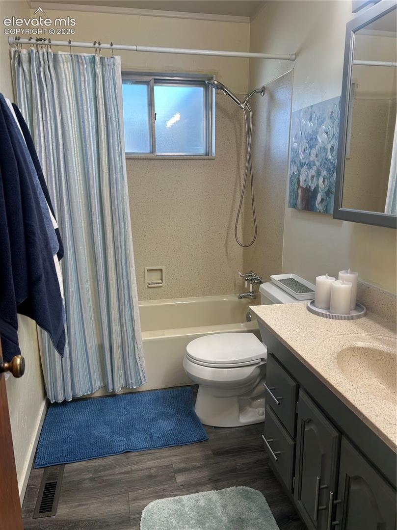 Bathroom featuring a grey vanity with a solid-surface countertop, integrated sink, shower and tub combination with a sliding window, and wood-finish flooring